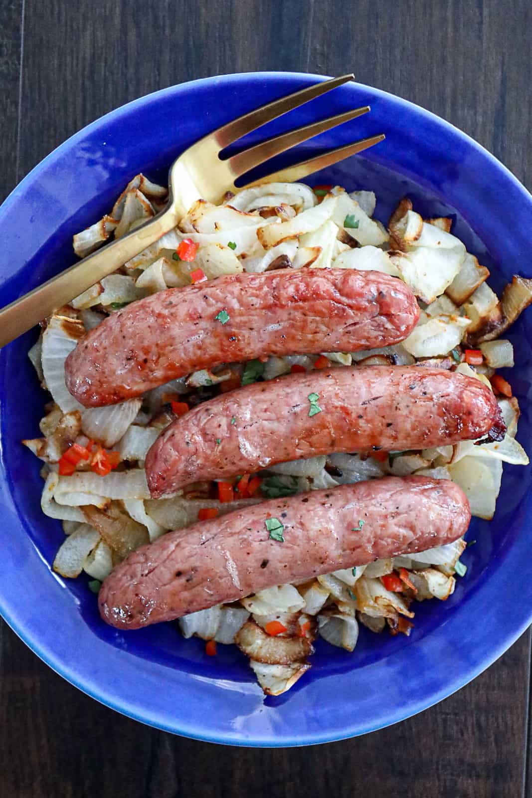 Air fryer beer bratwurst on a dinner plate with caramelized onions and peppers