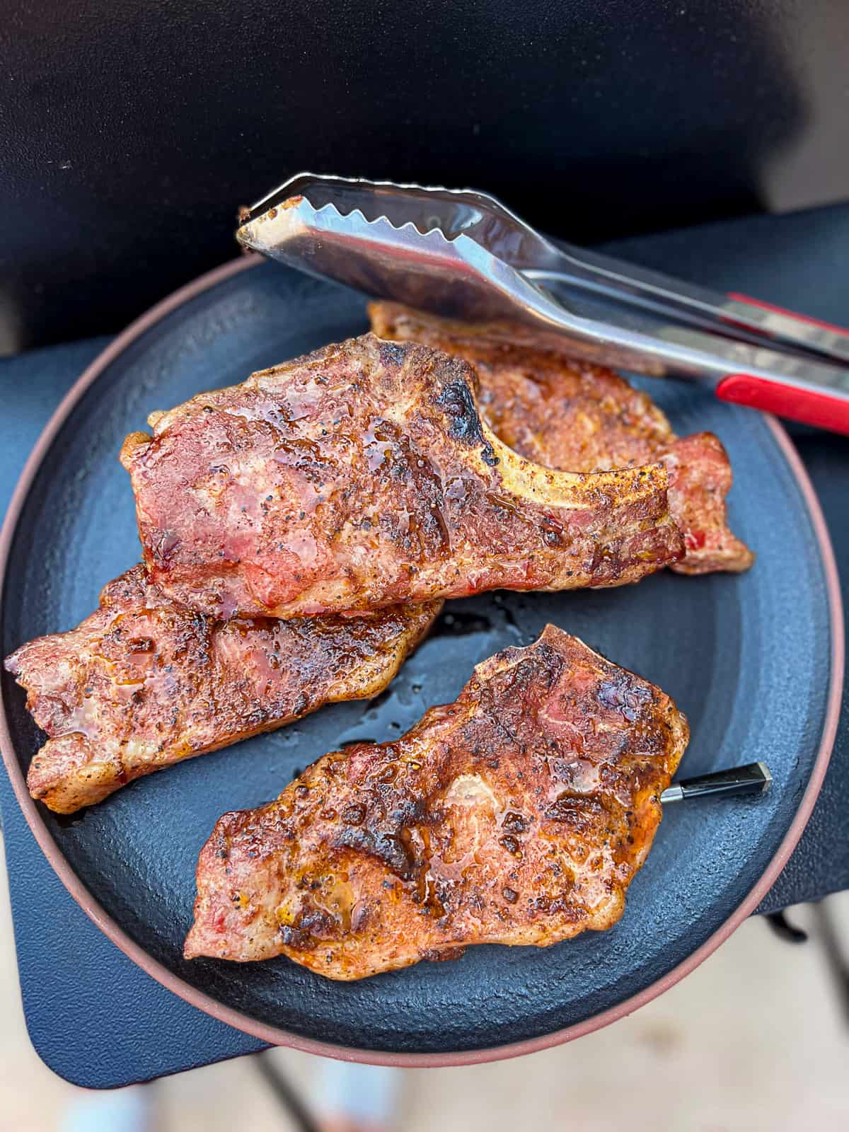 Juicy smoked Traeger Pork Chops bone in on a dinner plate with tongs