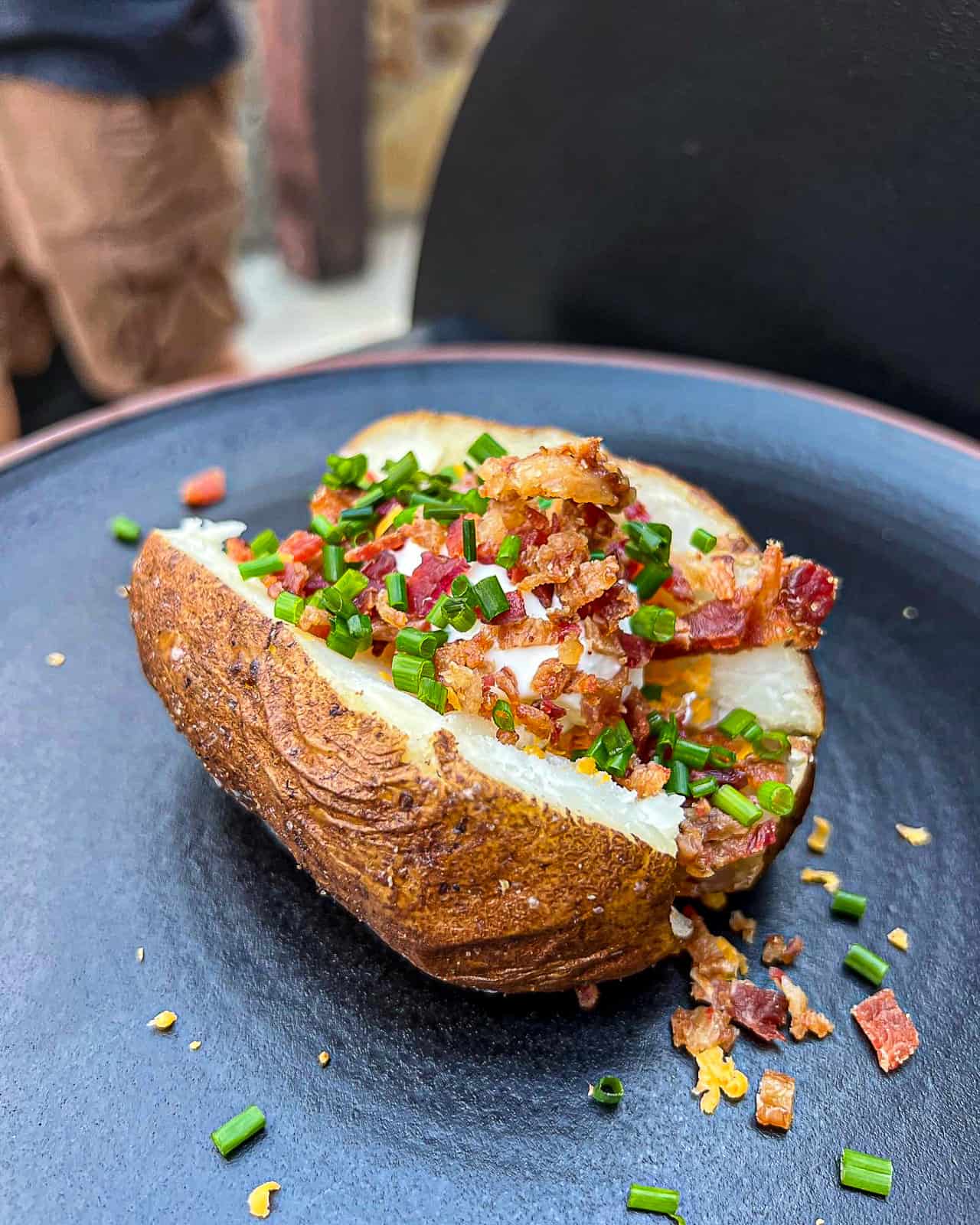 Smoked loaded baked potato with smoked bacon, chives, cream cheese, on a plate on the Traeger
