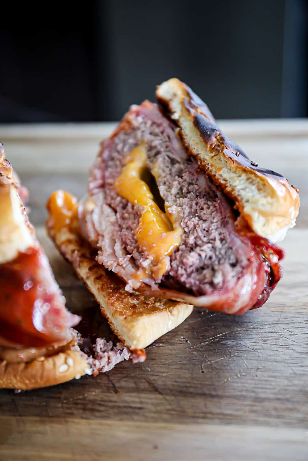 Cut In Half ½ LB burger patties smoked wrapped in bacon with cheese stuffed inside on a cutting board