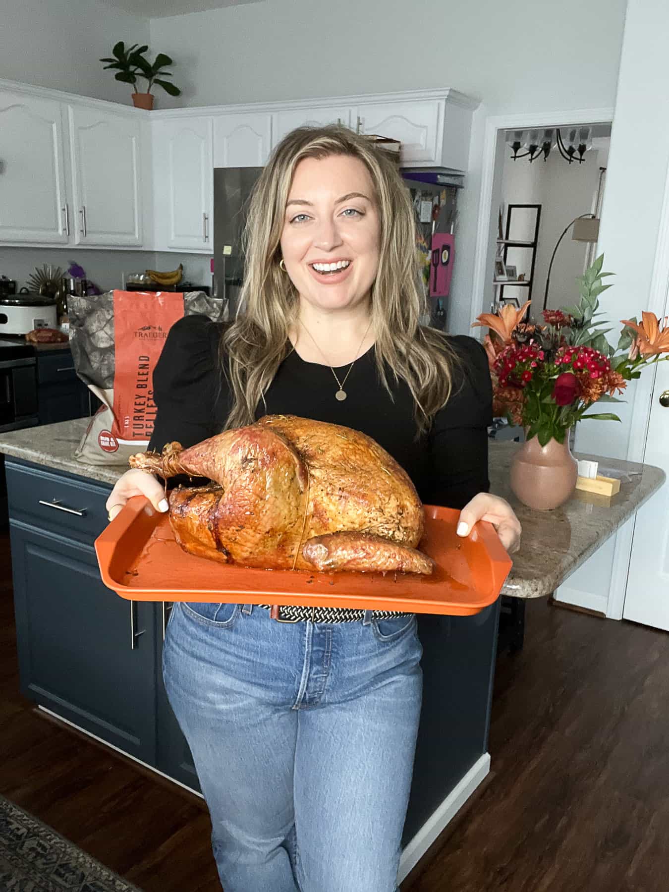 Jenna Passaro Food Blogger From Sip Bite Go Holding Smoked Thanksgiving Turkey Recipe With Bag Of Traeger Turkey Blend Pellets In The Kitchen