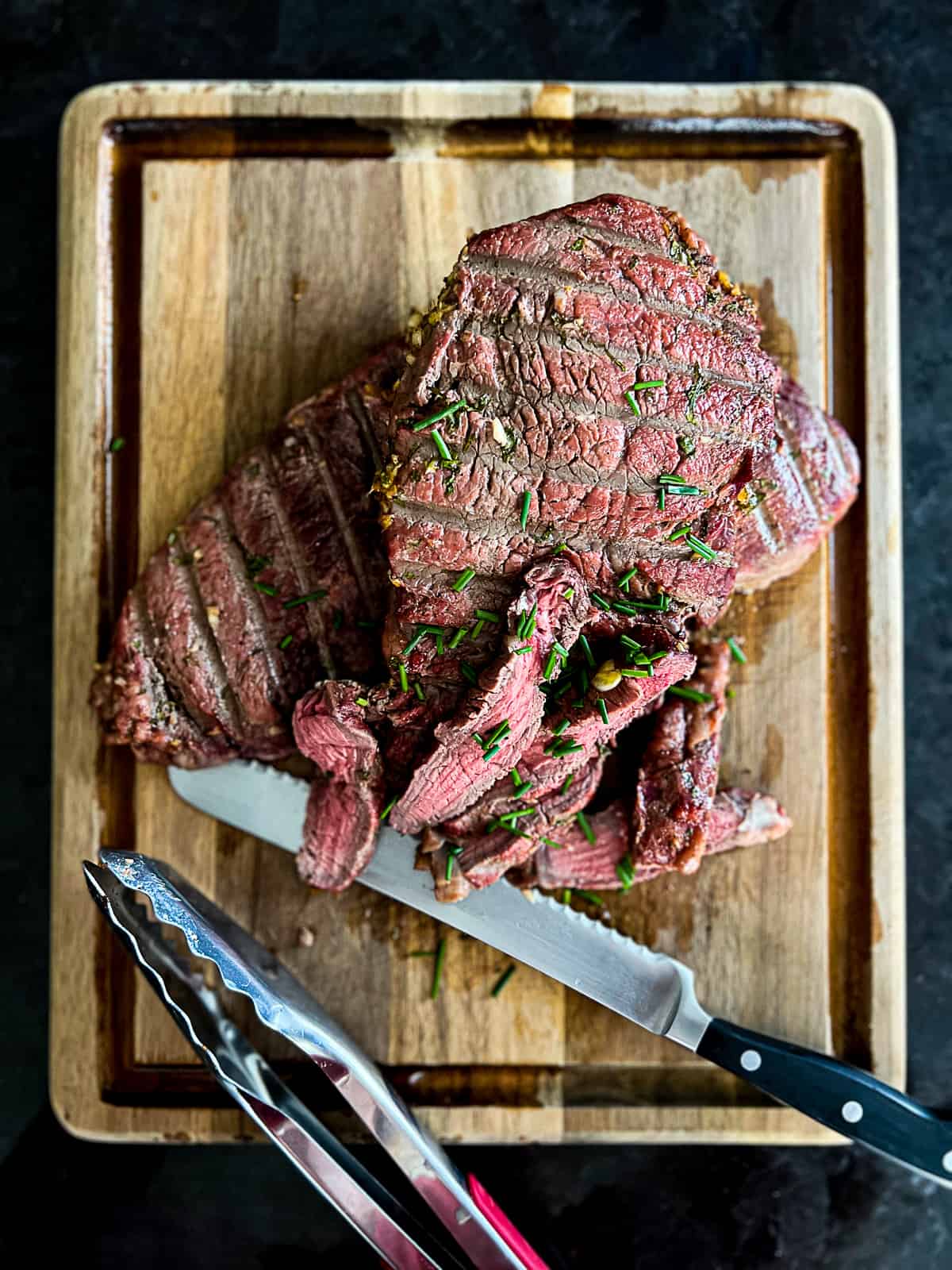 Sliced Traeger Sirloin Steak with fresh herbs and a cutting knife