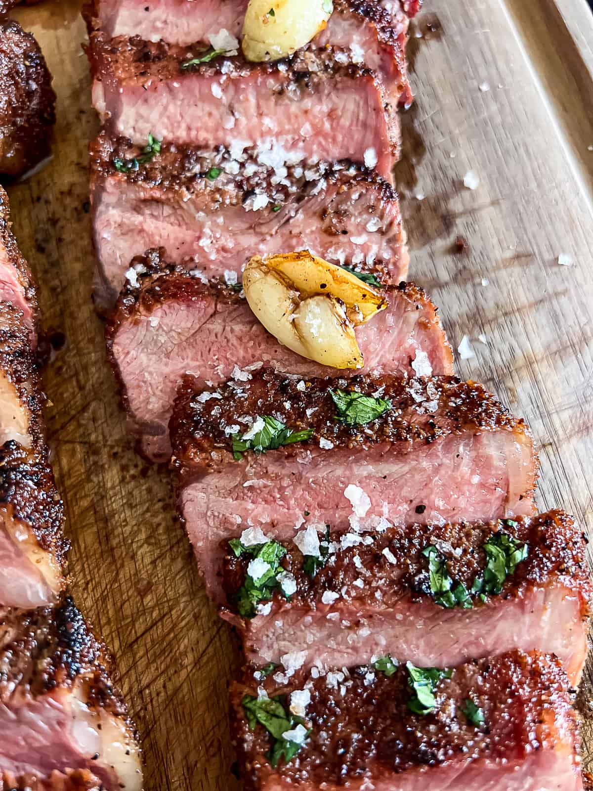 Closeup of roasted garlic on reverse seared Traeger New York Strip Steak smoked on the pellet grill with herbs and salt on top