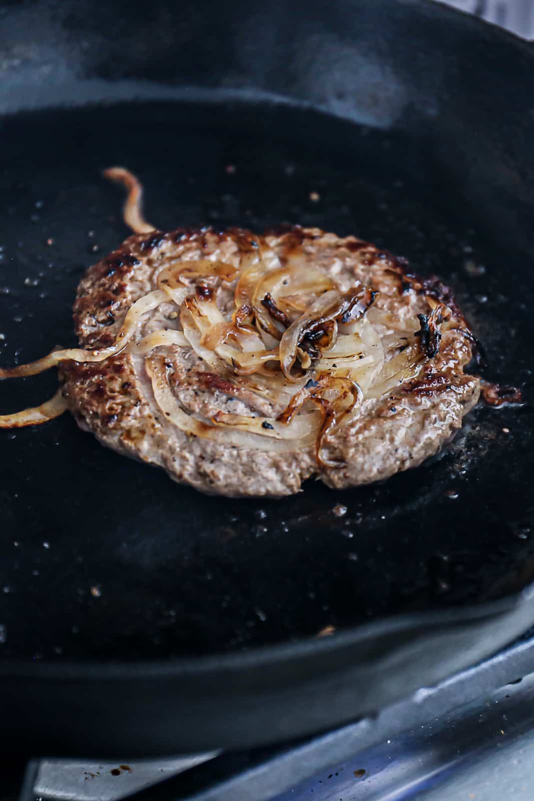 Oklahoma Onion Smash Burger Recipe Searing In A Cast Iron Skillet On The Stove
