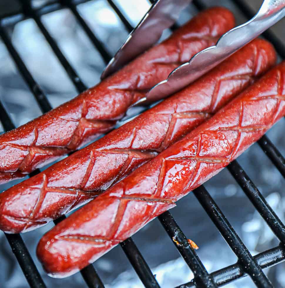 Traeger Smoked Hot Dogs With Tongs On Grill Grates
