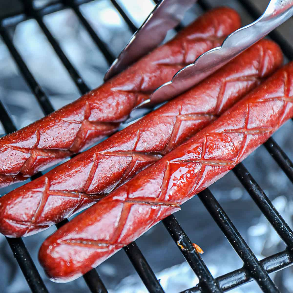 Traeger Smoked Hot Dogs With Tongs On Grill Grates 