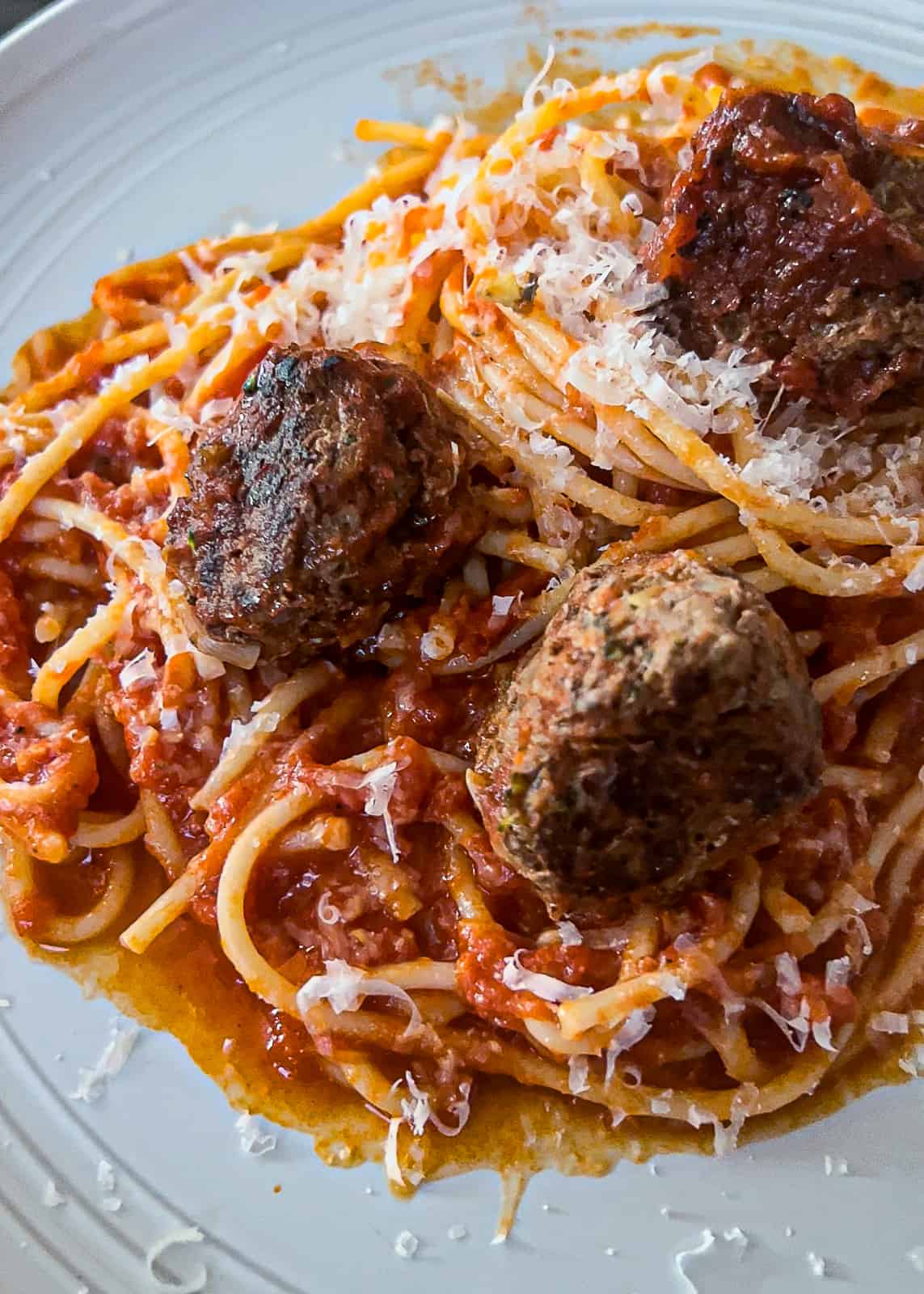cooked veggie and ground beef meatballs with spaghetti and parmesan cheese on a dinner plate