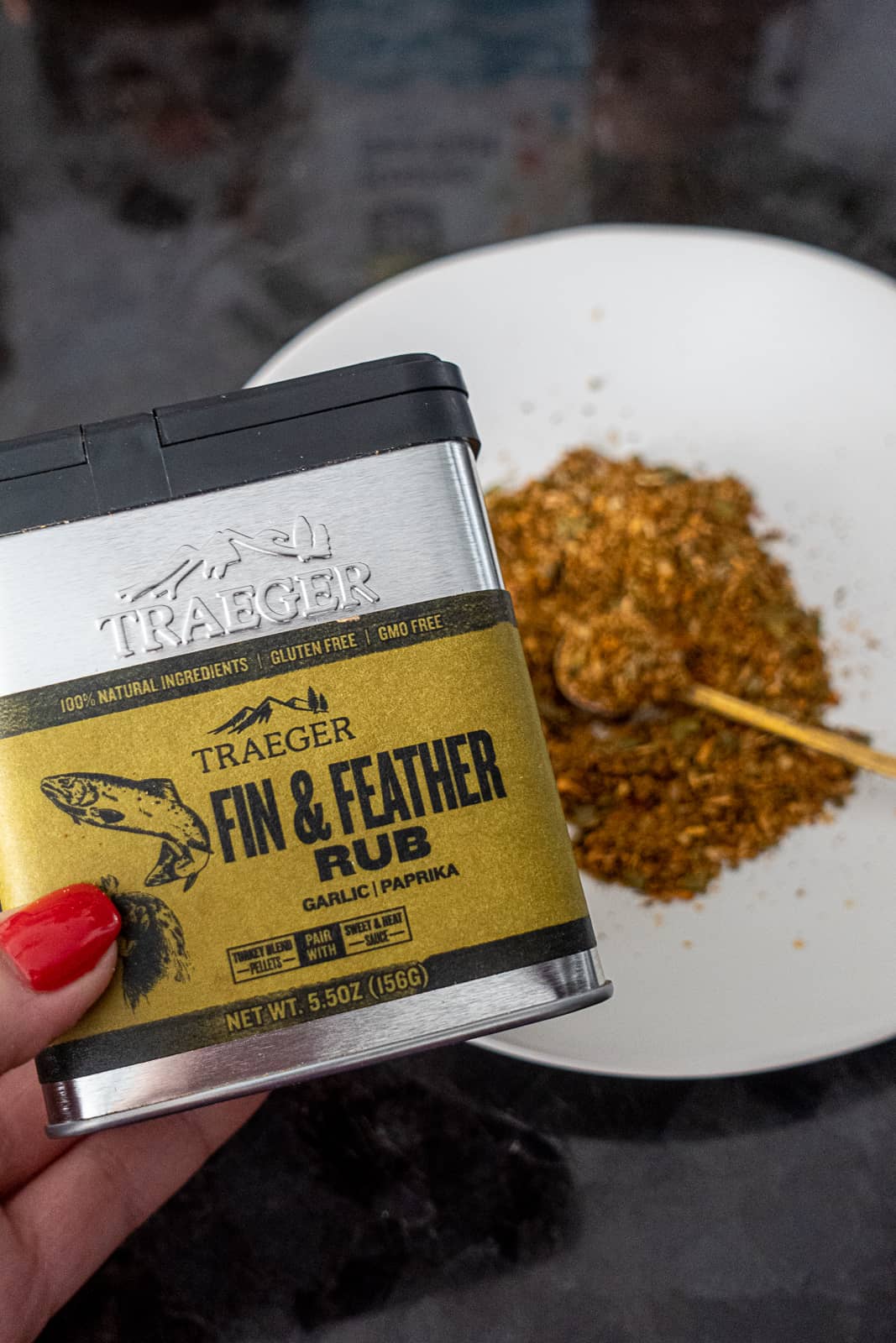 Can of Signature Traeger Fin And Feather Rub with spices on plate in background