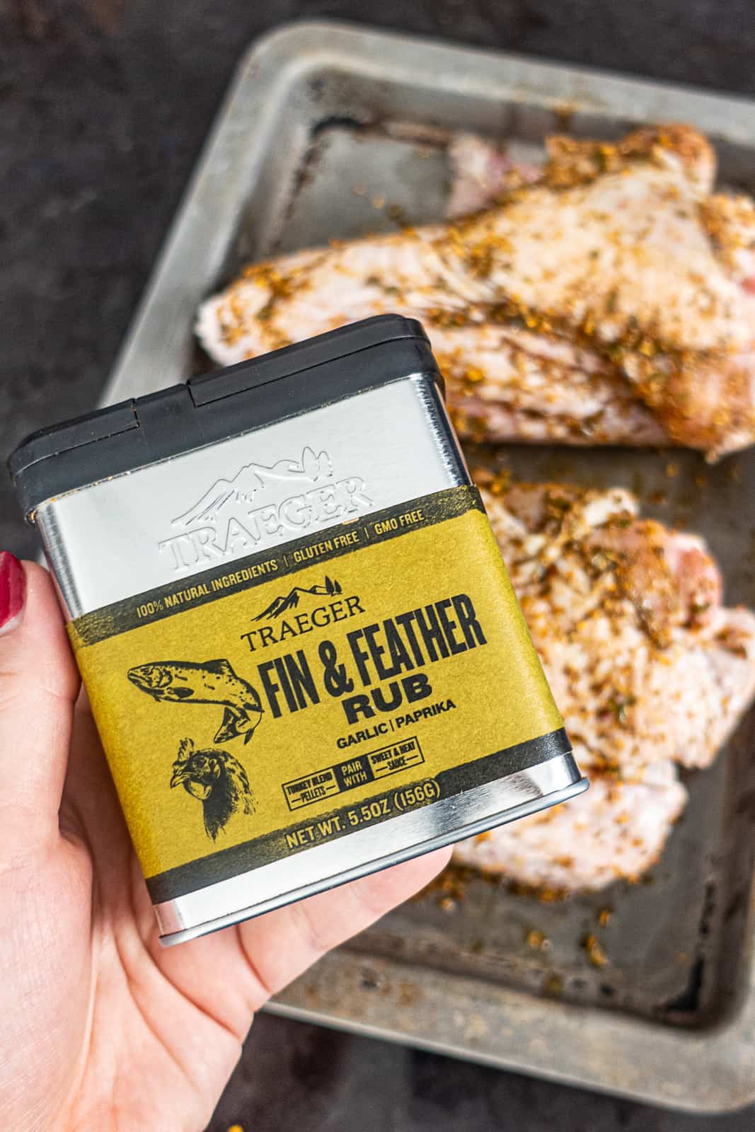 Holding Traeger Fin And Feather Rub Spice Container with seasoned turkey wings for smoking