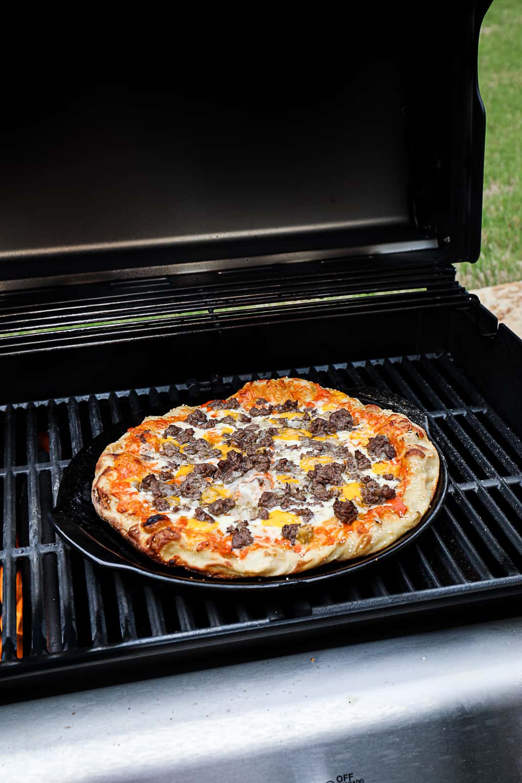 Grilling Pizza with cheeseburger toppings including mustard and pickles