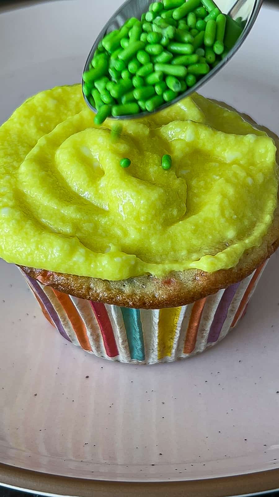 Adding grass sprinkles to Funfetti Easter Cupcakes with yellow frosting