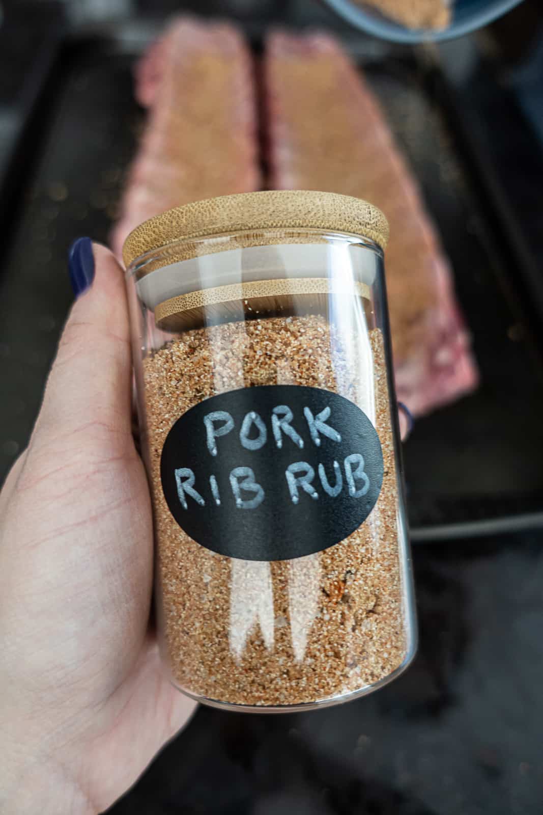 Hand holding pork rib rub infront of ribs