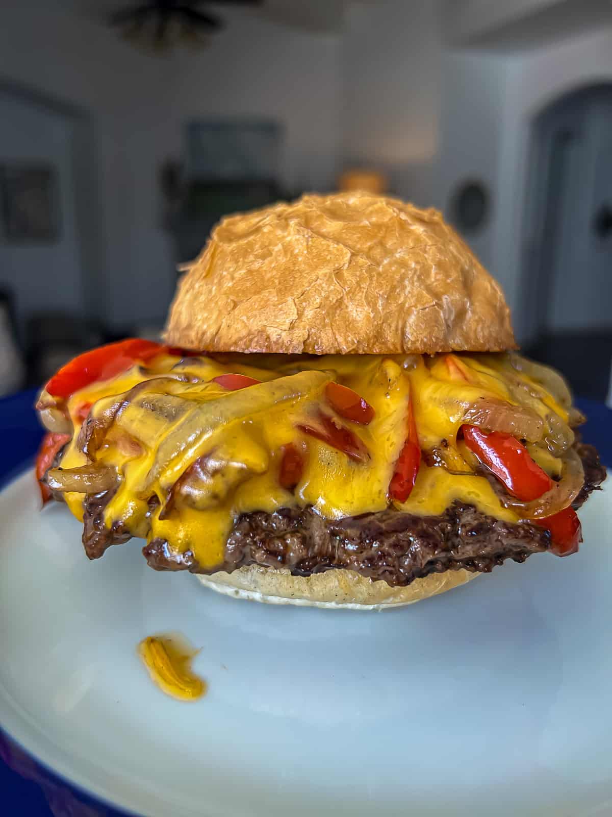 Smashed Philly cheesesteak burger with melted cheddar cheese and onions and peppers on a plate