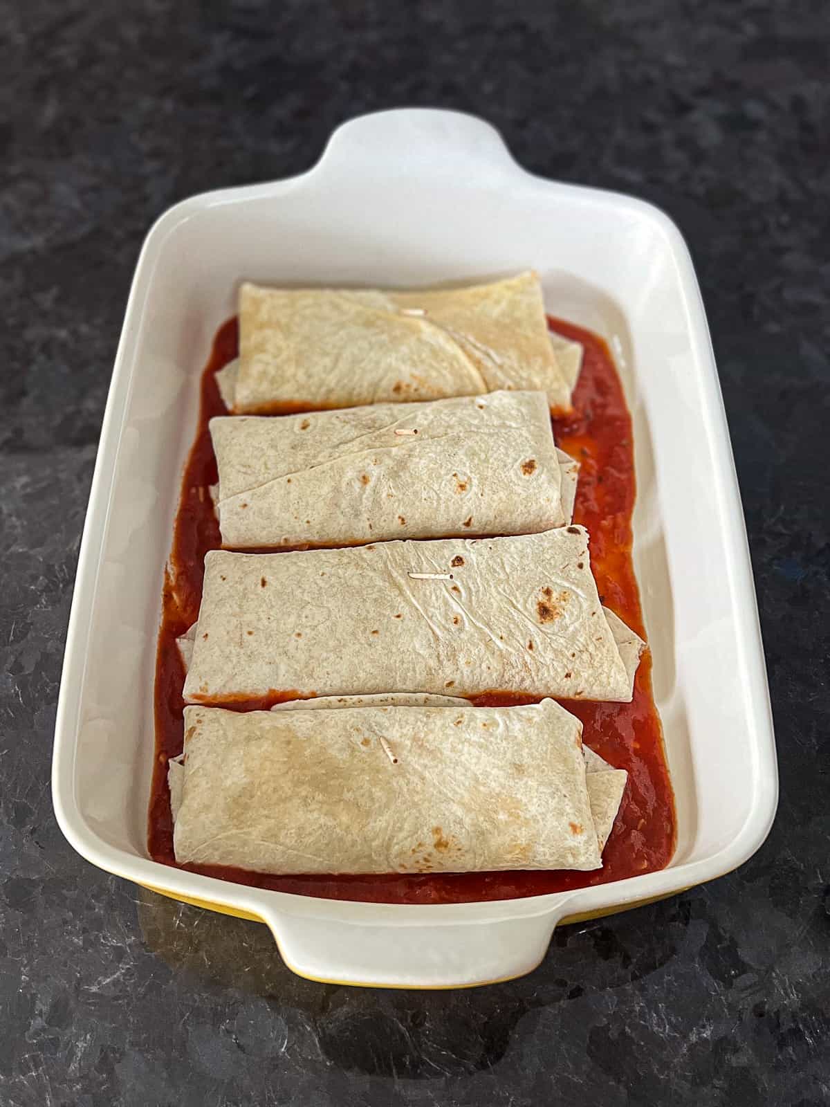 Homemade Red Enchilada Sauce in baking dish with enchiladas prepped in tortillas