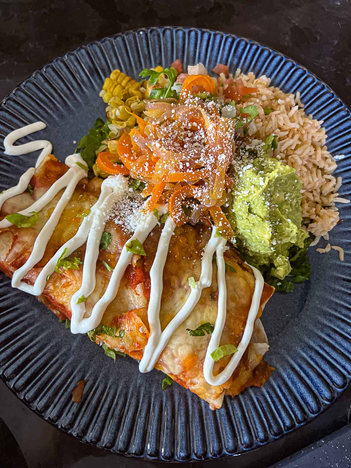 Closeup of Chicken Enchiladas with sides including rice and guacamole on a dinner plate