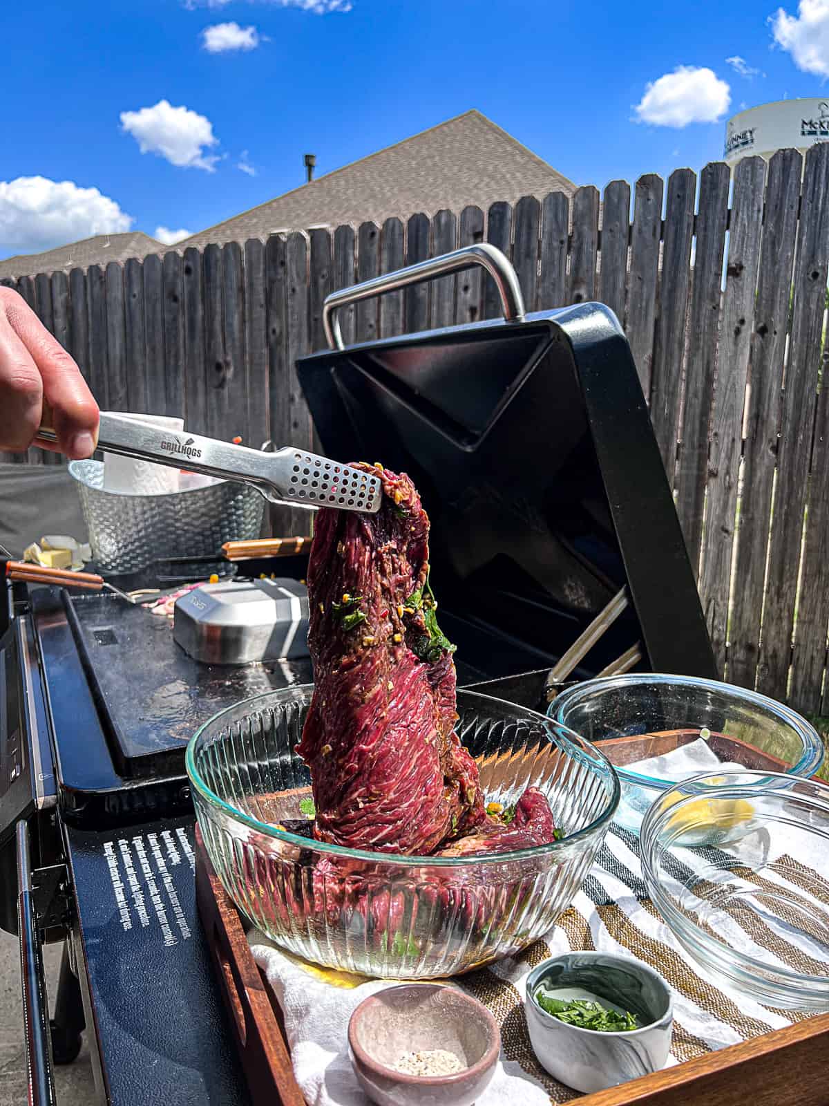 Tongs pulling tenderized flap meat out of marinade next to Traeger Flatrock Griddle Grill