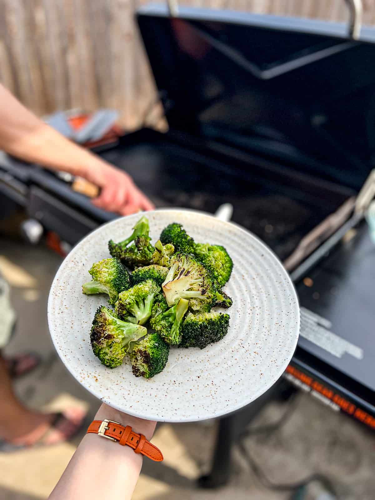 Holding Griddled Broccoli Recipe in front of Traeger Flatrock Griddle Grill