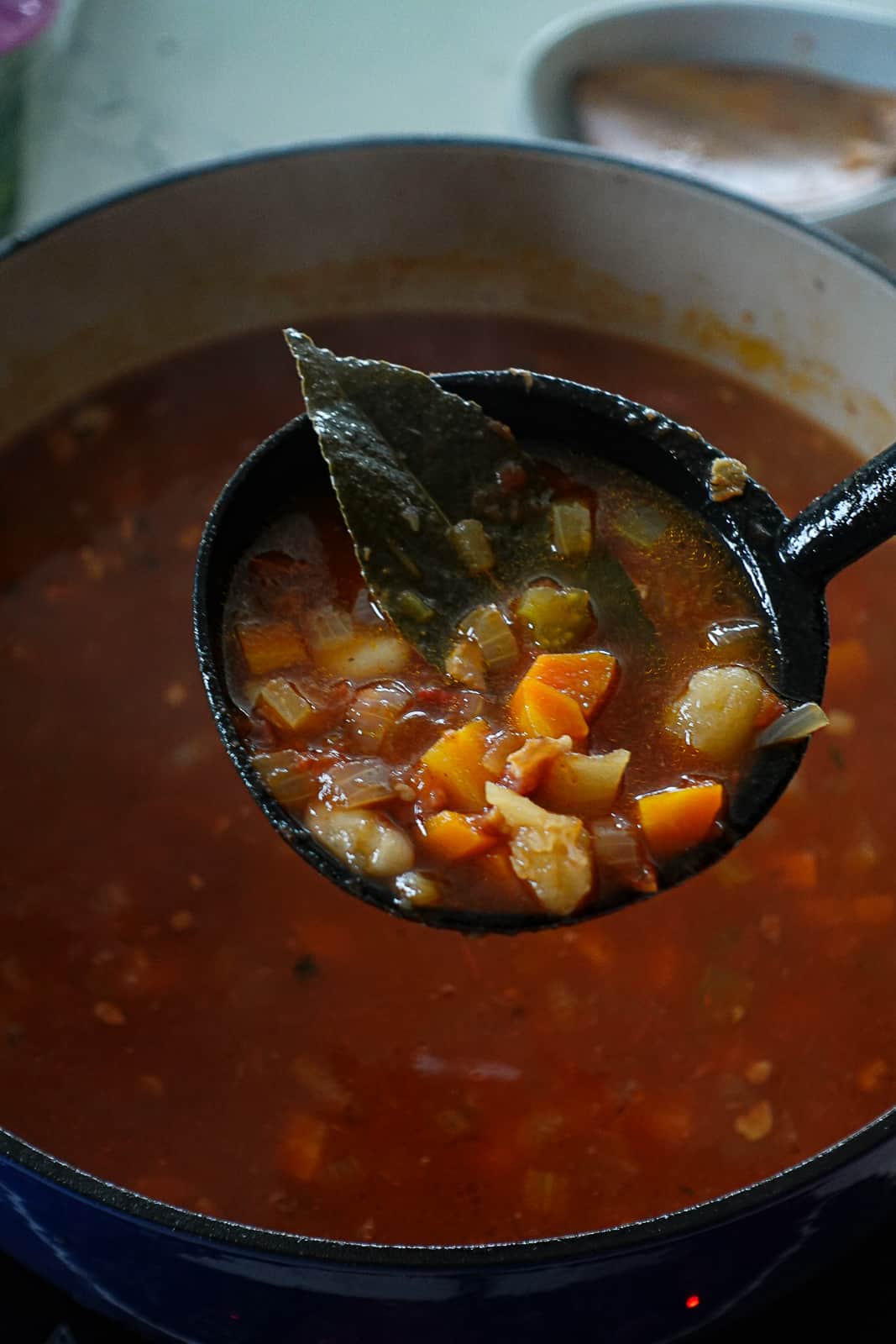 Minestrone Soup Broth cooking with spoon holding vegetables and bay leaf