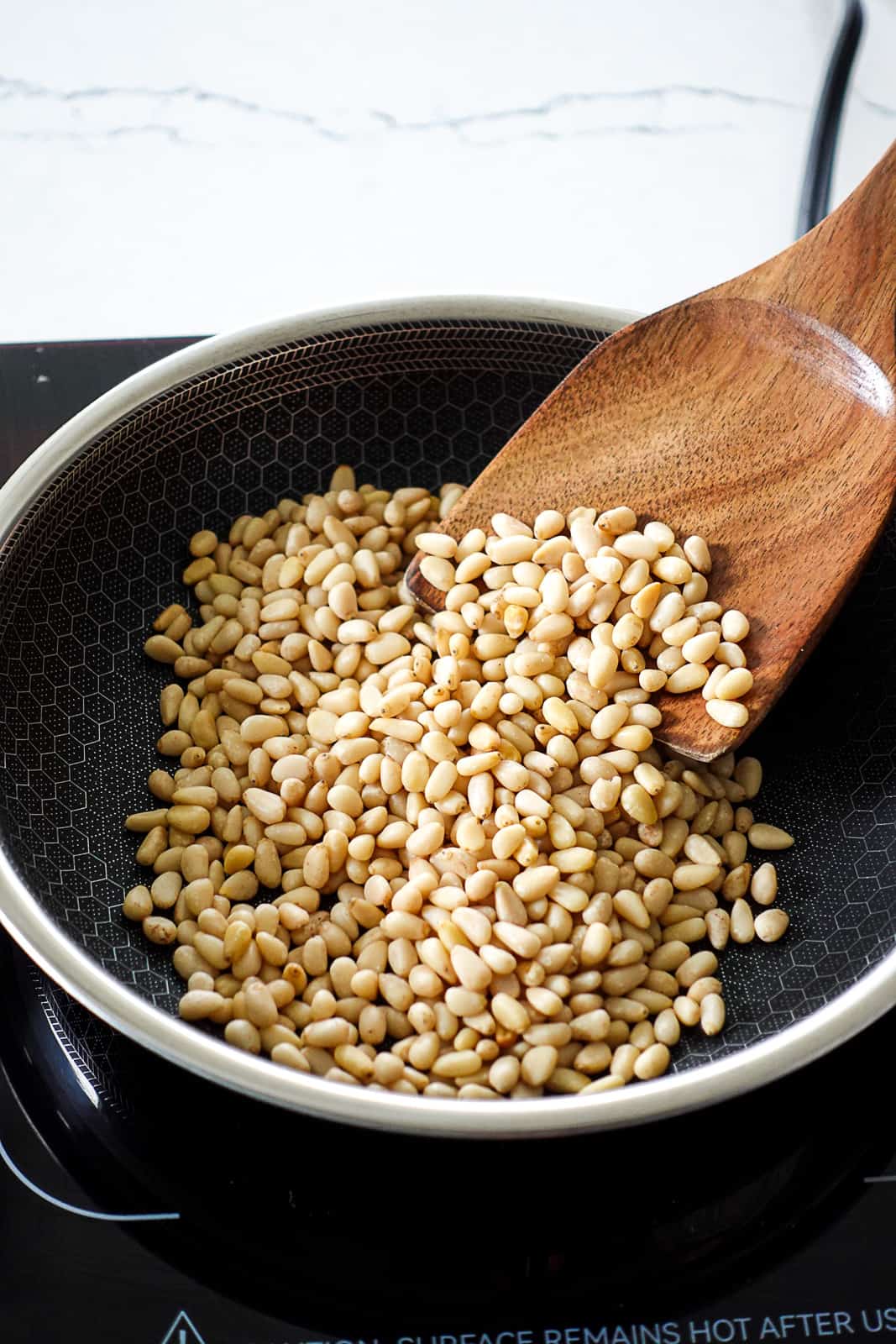 Raw Pine Nuts Toasting in a Hexclad Pan with a wooden spatula