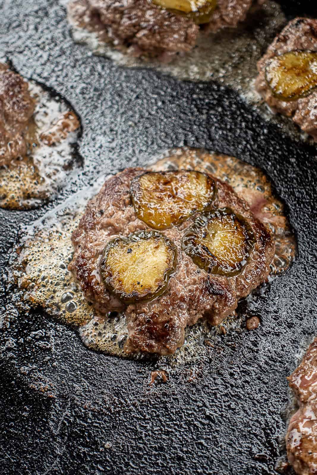 Closeup of Griddle Cooking Smash Burgers with Pickles