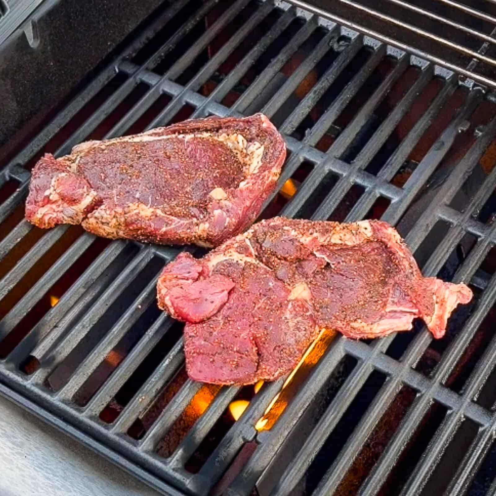 Seasoning ribeye steaks evenly with BBQ seasoning