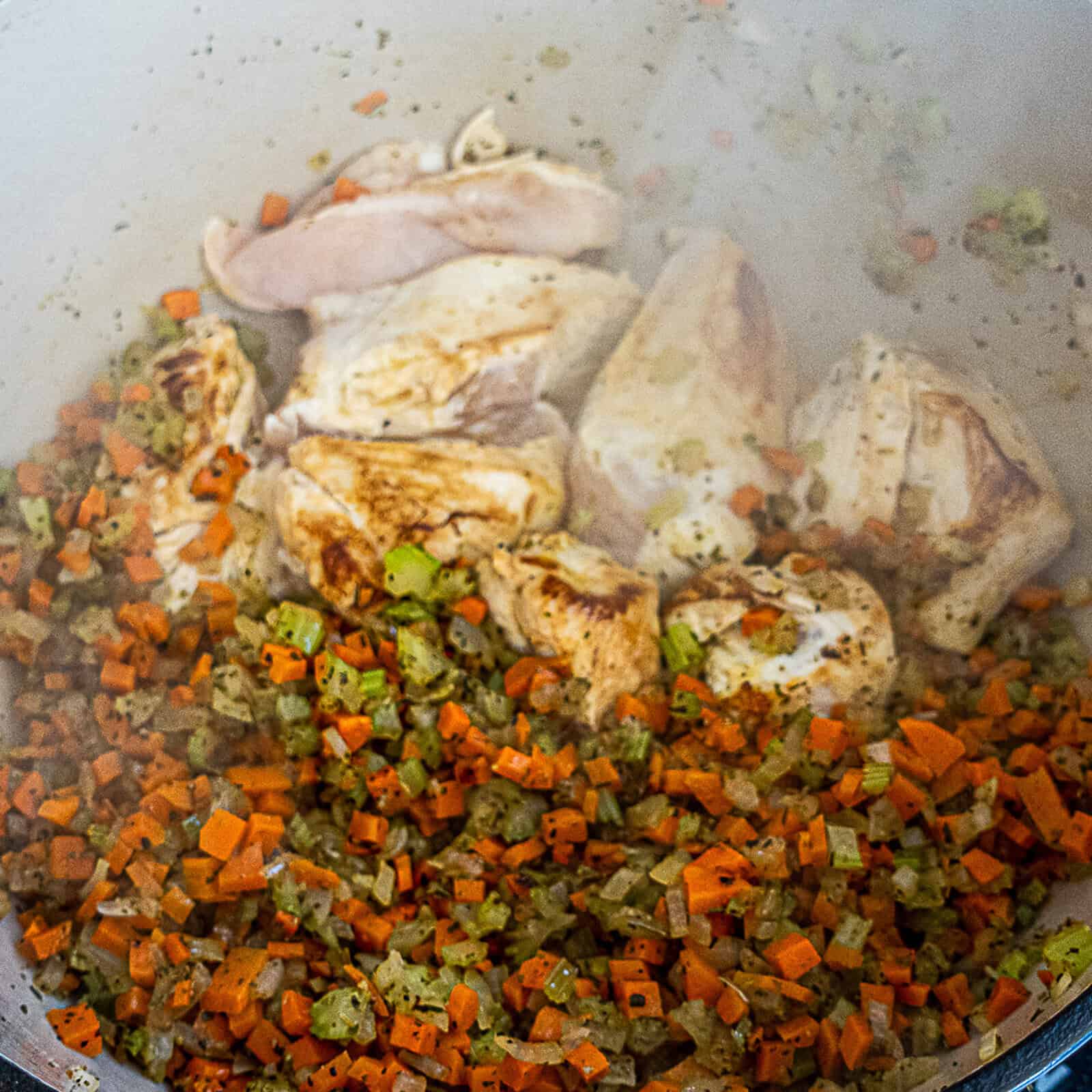 Cooking chicken breast pieces in a soup pot with sautéed vegetables