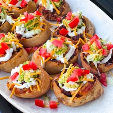 Freshly Traeger smoked or oven baked taco pizza rolls topped with sour cream, guacamole, shredded lettuce, cheese, diced tomato, and onion, arranged on a white platter