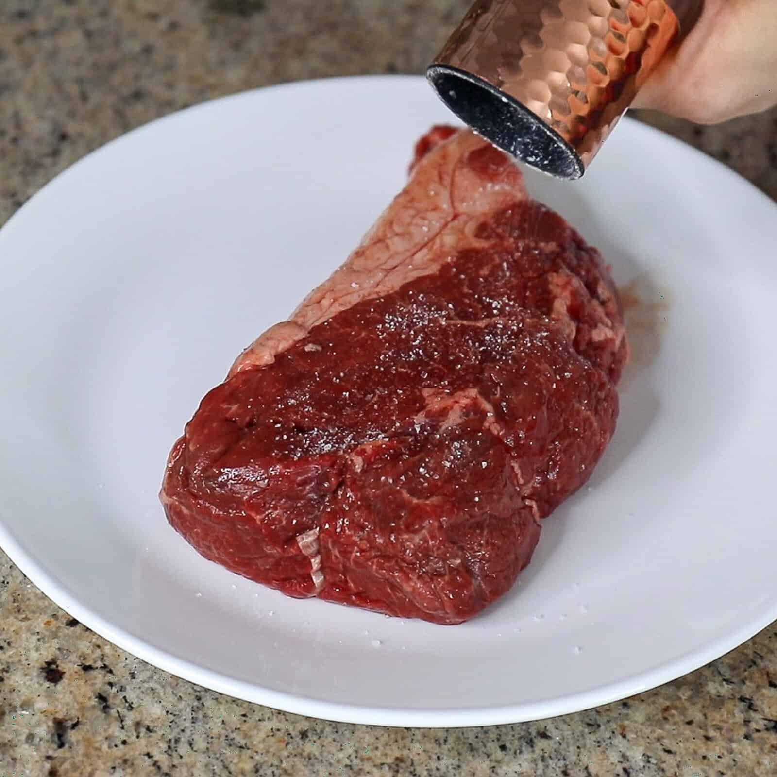Seasoning top sirloin steak with salt and pepper before cooking