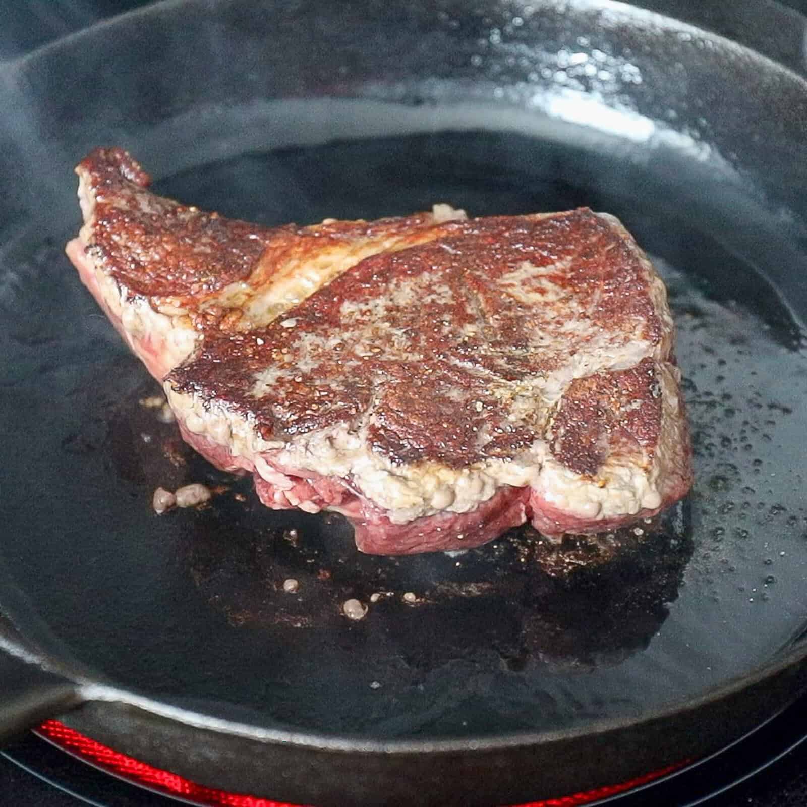 Flipping a sirloin steak in a pan to sear the other side