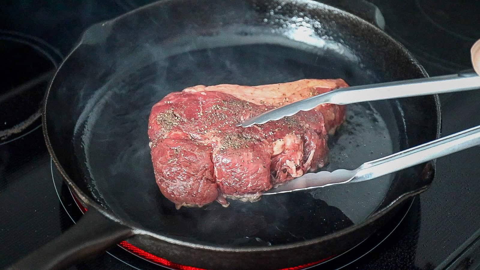 Searing a sirloin steak on a pan before finishing in the oven