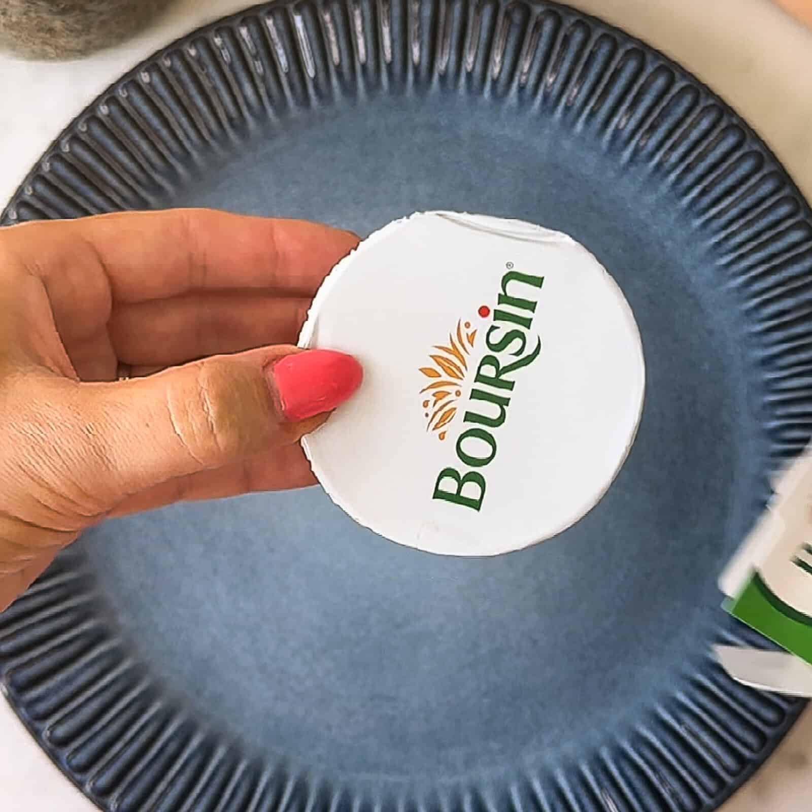 hand holding a store-bought packaged Boursin cheese puck