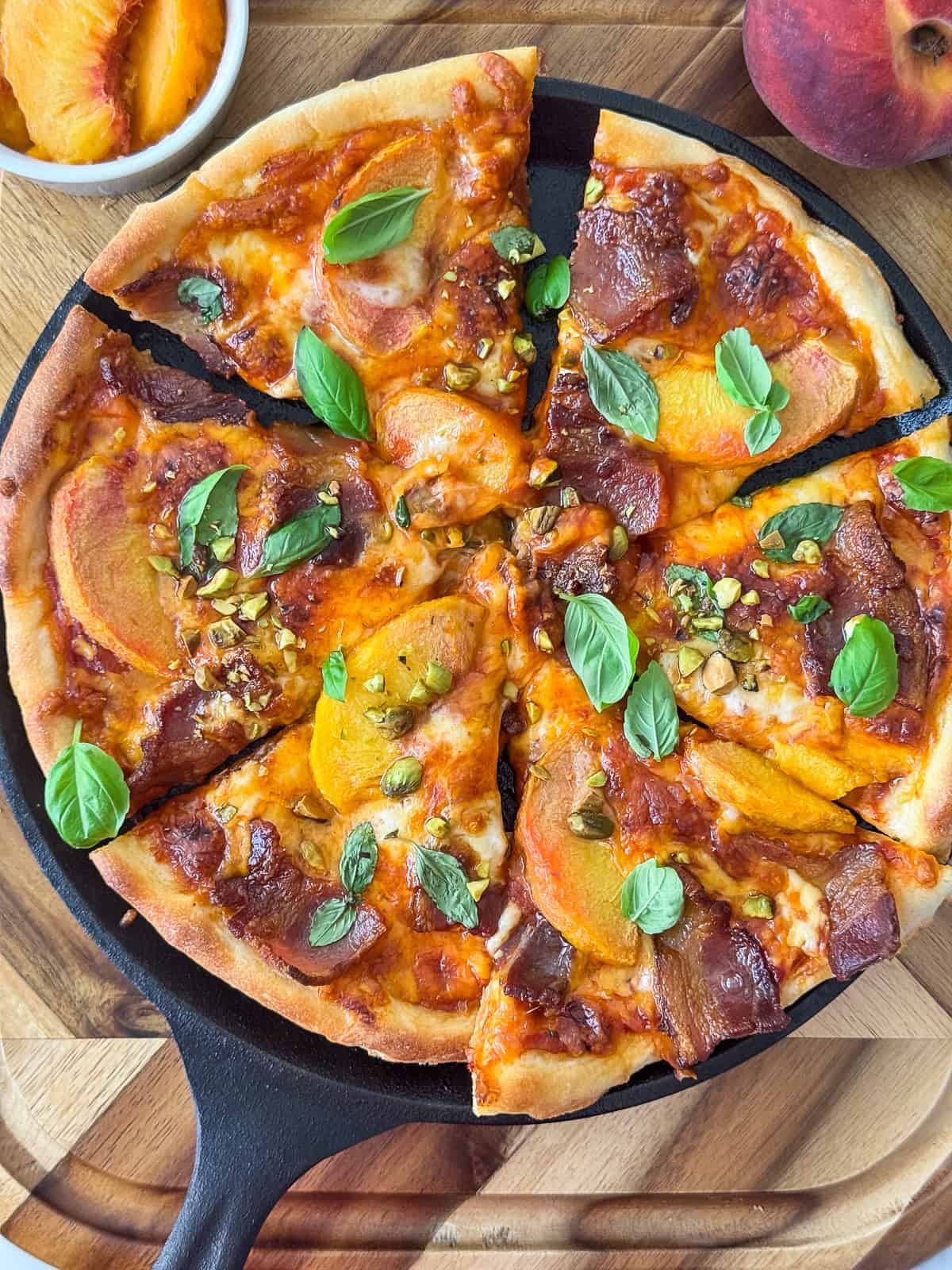 Closeup of peach and bacon pizza topped with pistachios and basil