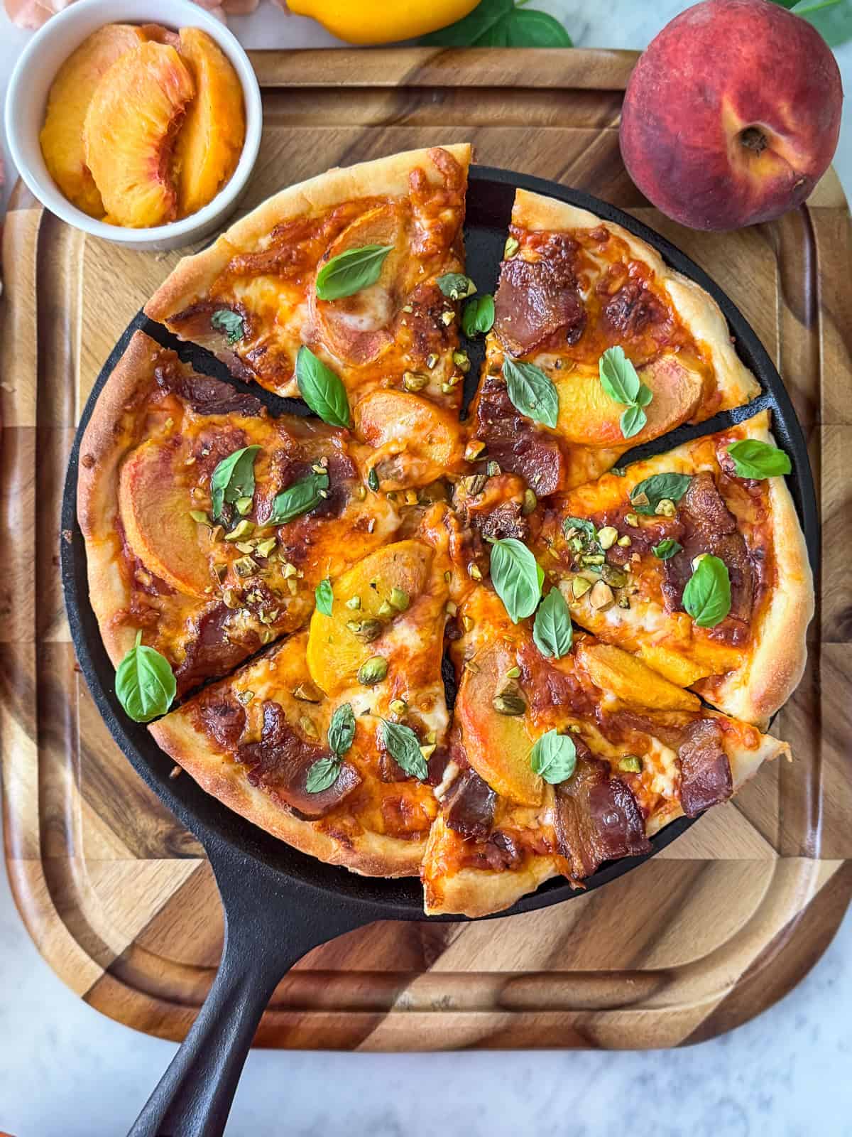 Fresh peaches next to a peach and bacon pizza on a cutting board
