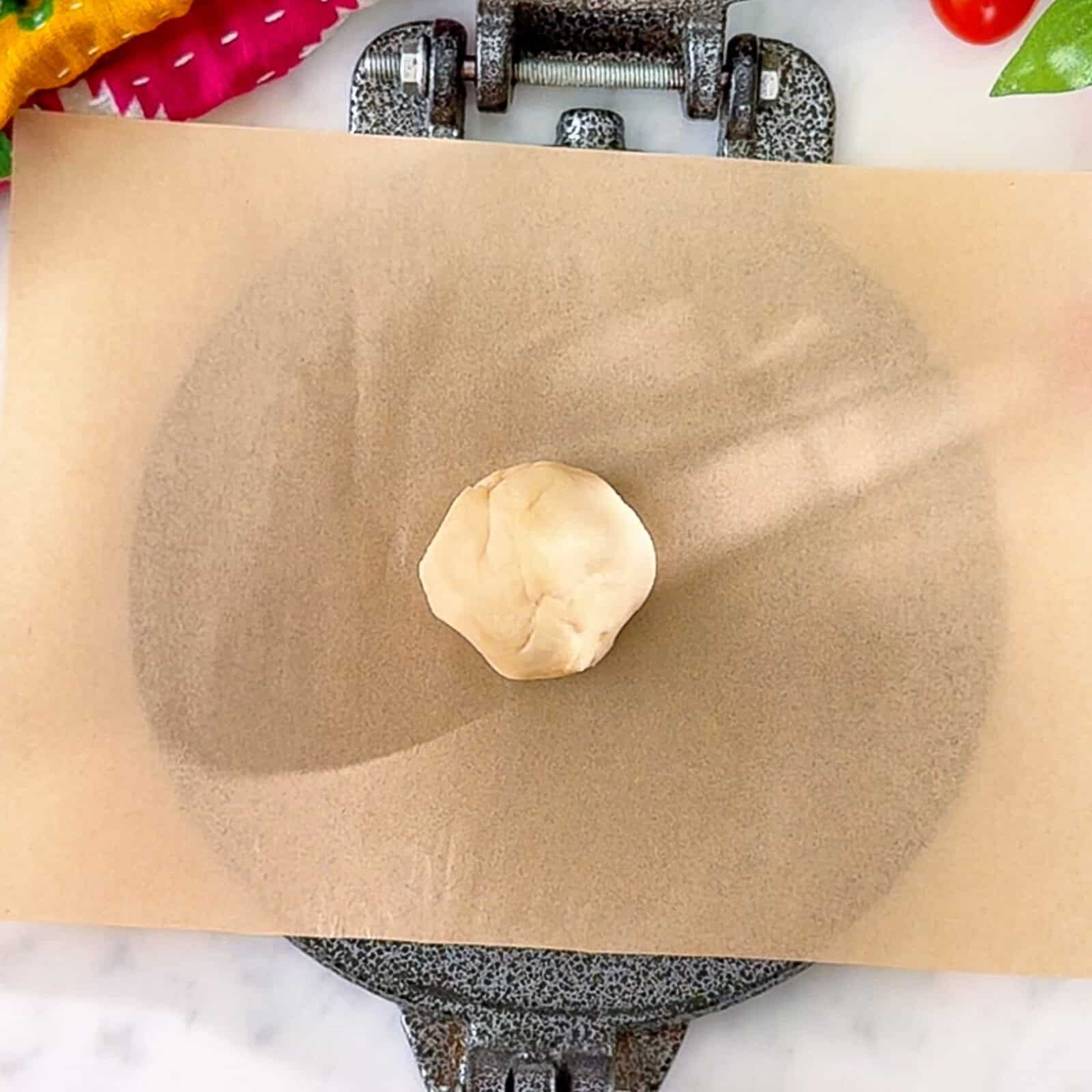 dough ball for butter tortilla placed on parchment paper inside a tortilla press