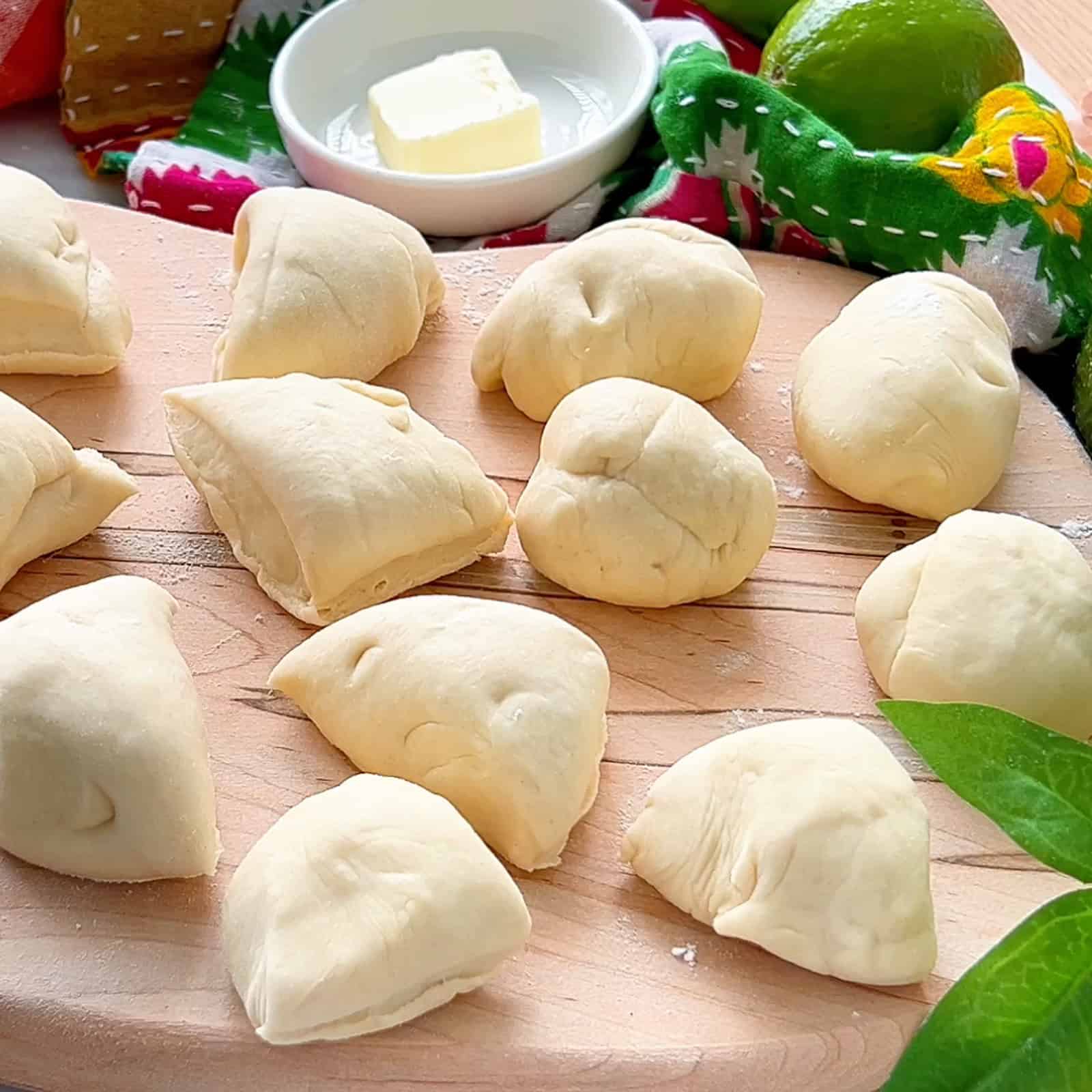 butter tortilla dough balls resting on a wooden cutting board with a colorful mexican towel in the background