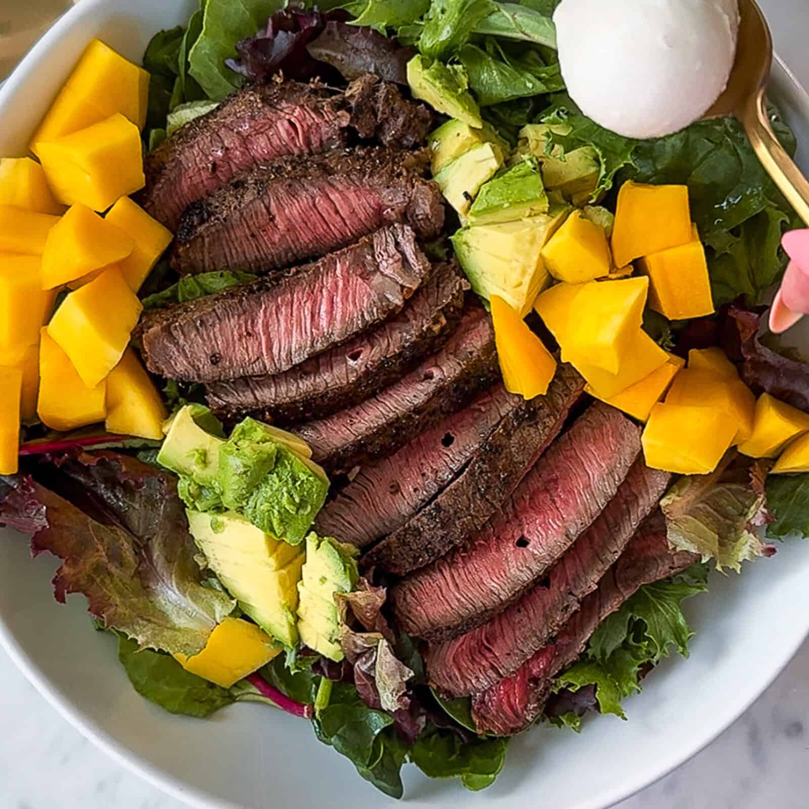 Placing cooked steak slices on top of mixed salad greens