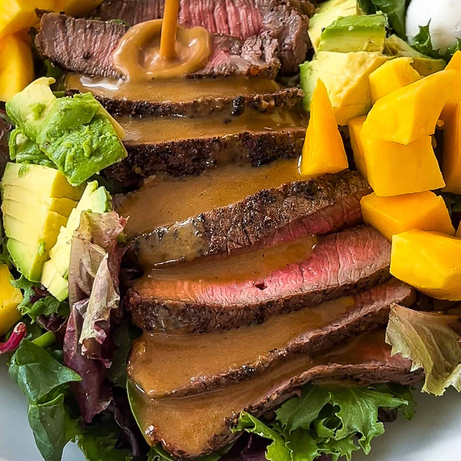 Pouring balsamic dressing over a steak and mango salad