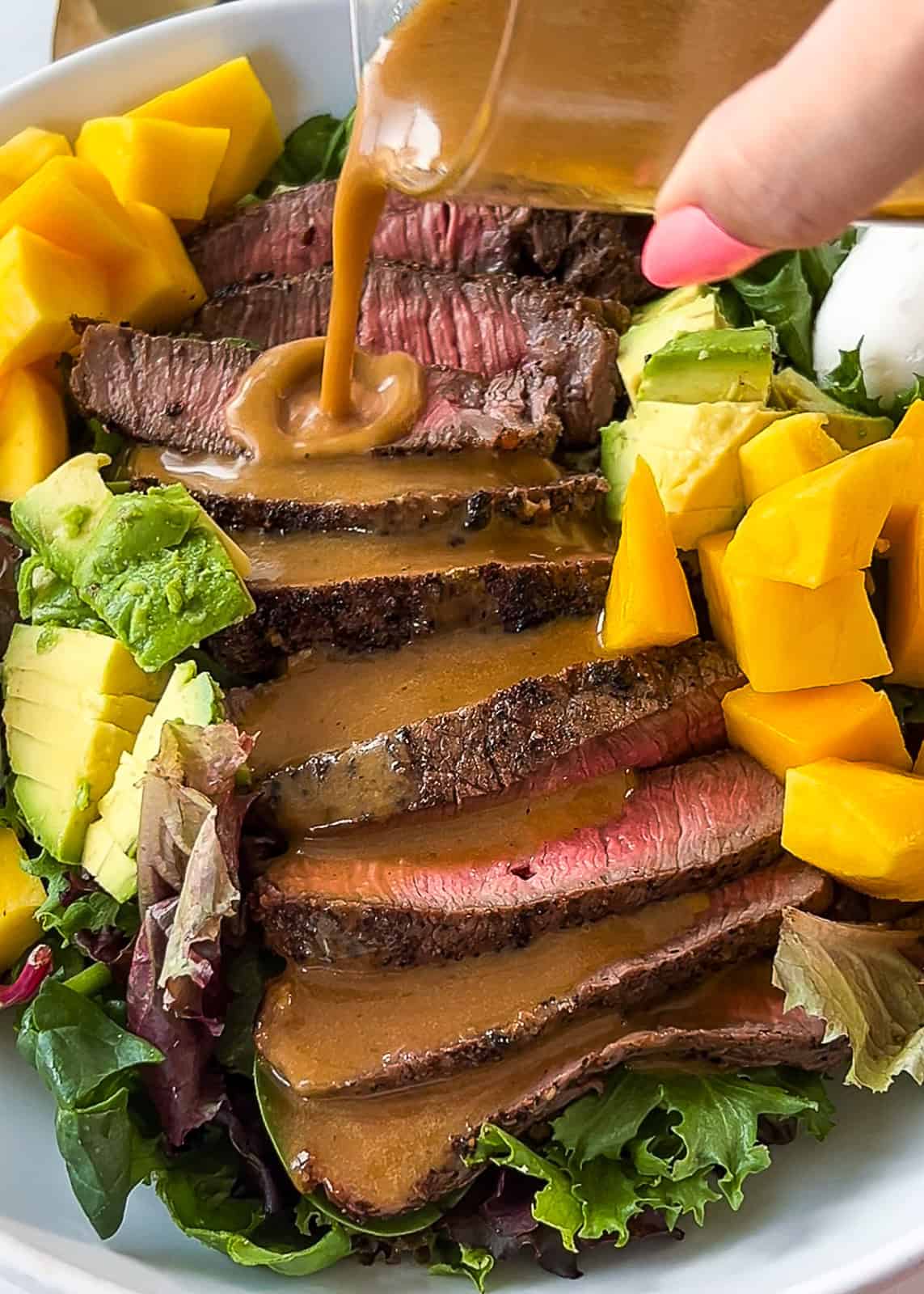 Grilled steak arranged on top of greens and mango salad