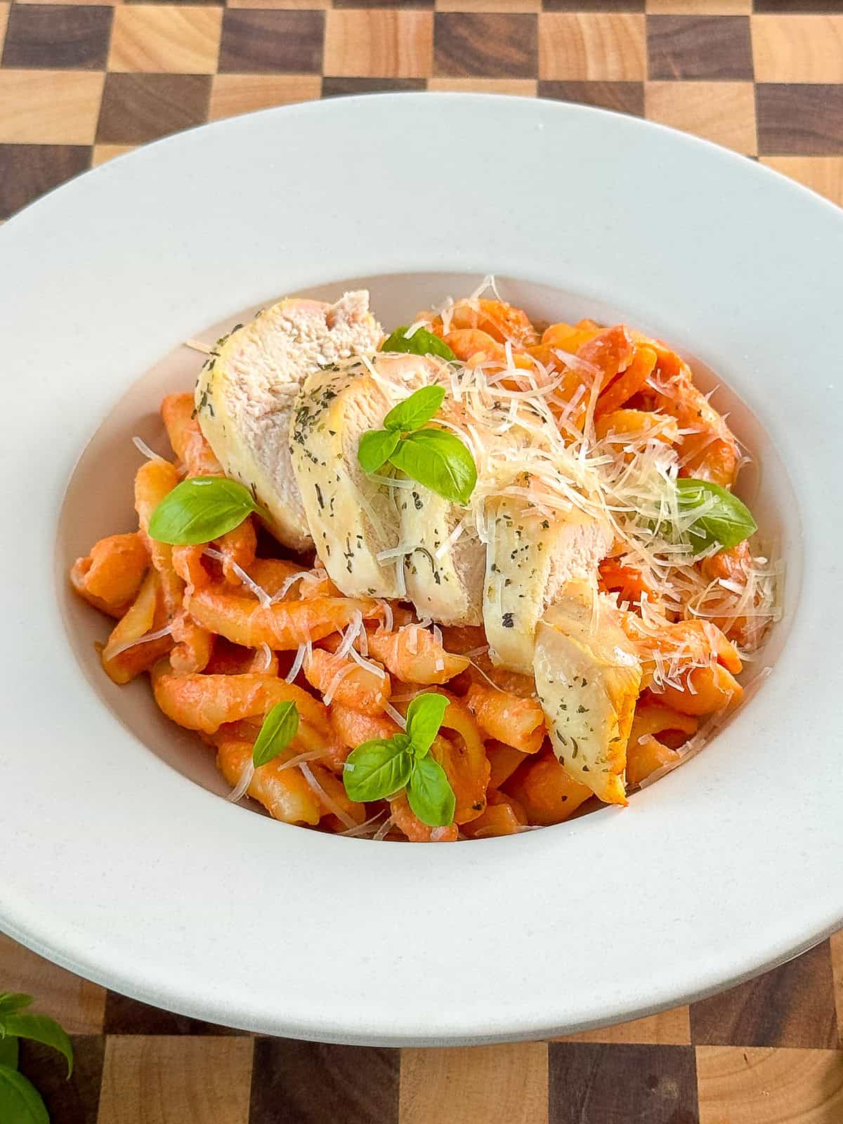 Closeup of fresh basil and grated Parmesan on top of creamy tomato mozzarella pasta with chicken