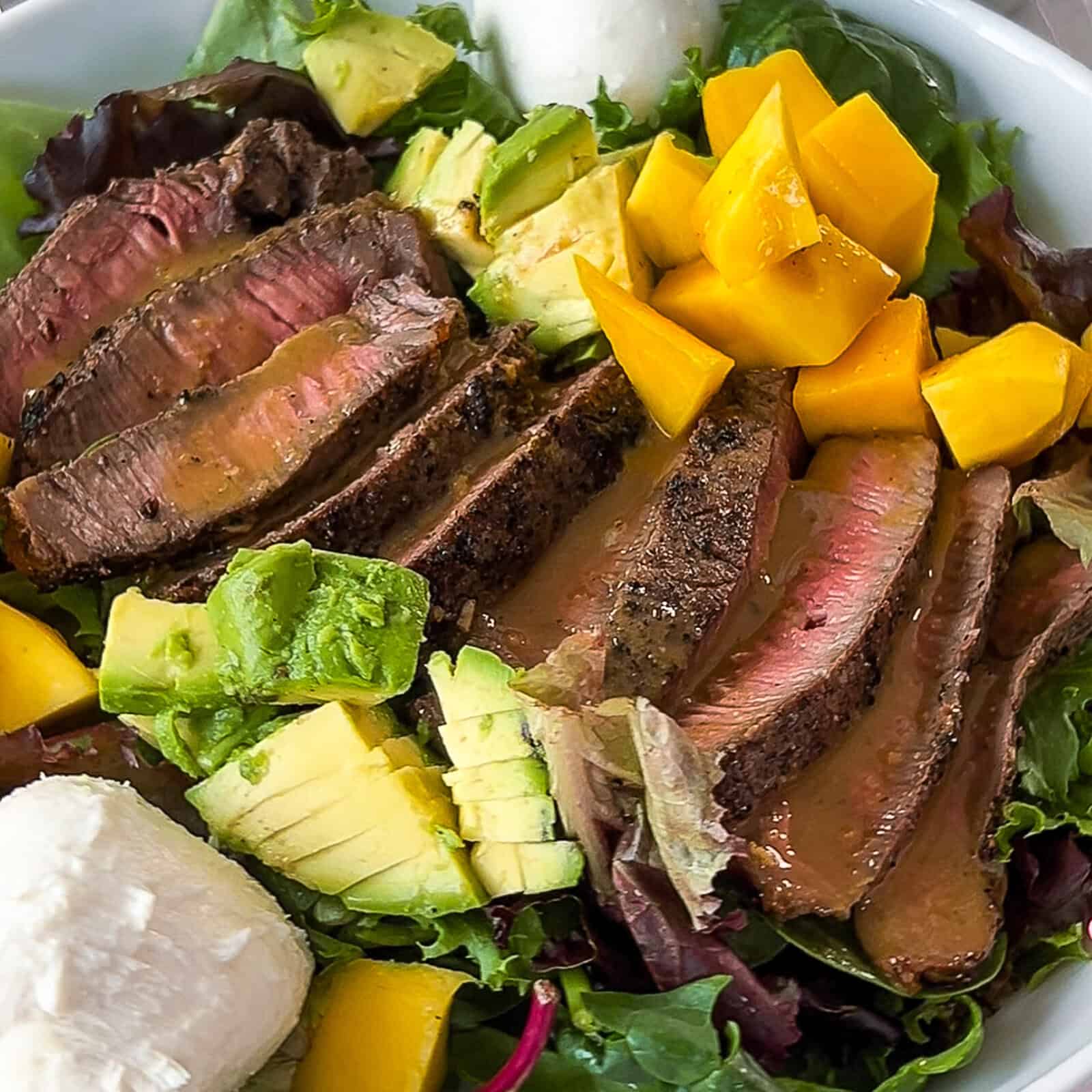 Serving a fresh steak salad topped with mango and avocado