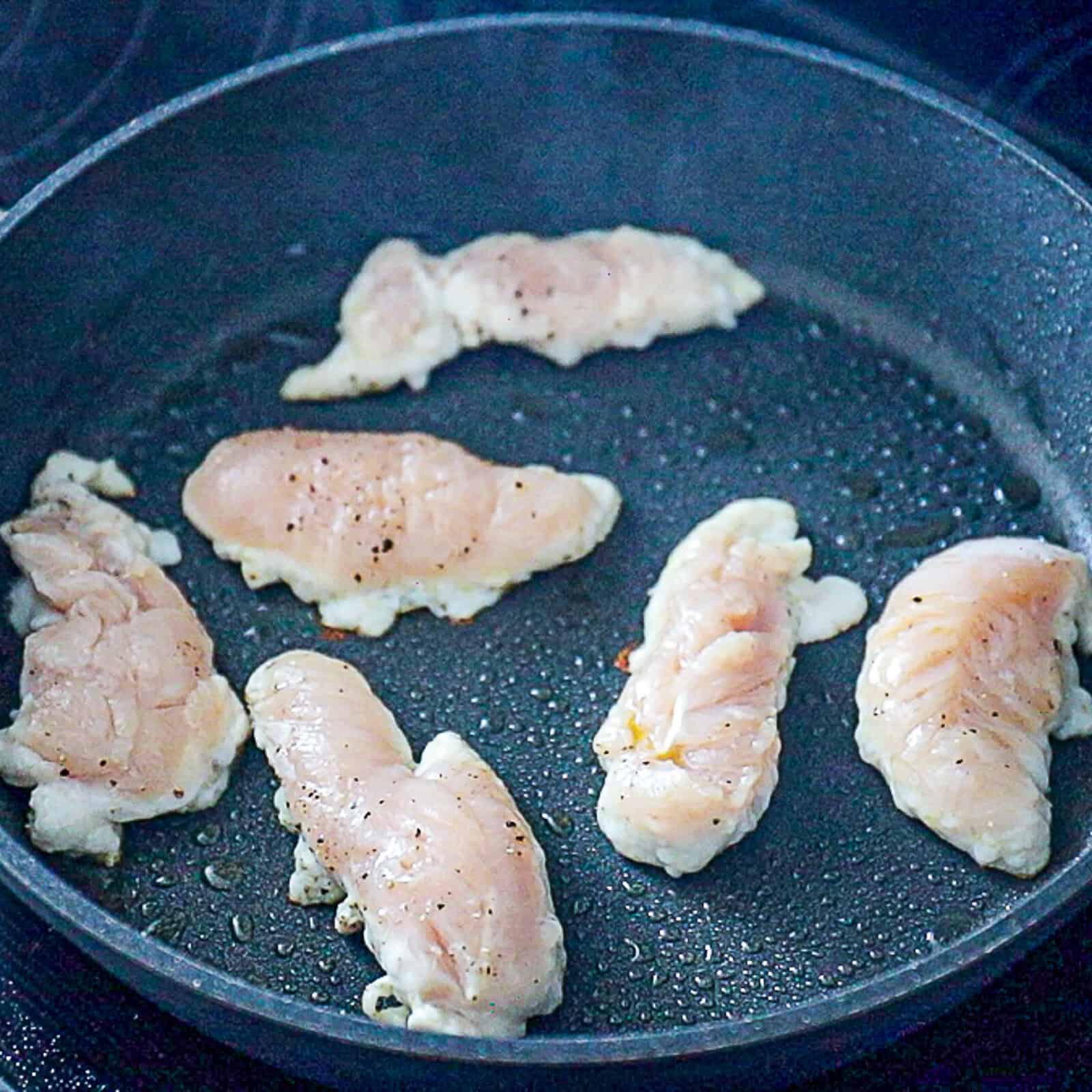 Chicken tenderloins searing in a hot skillet with olive oil