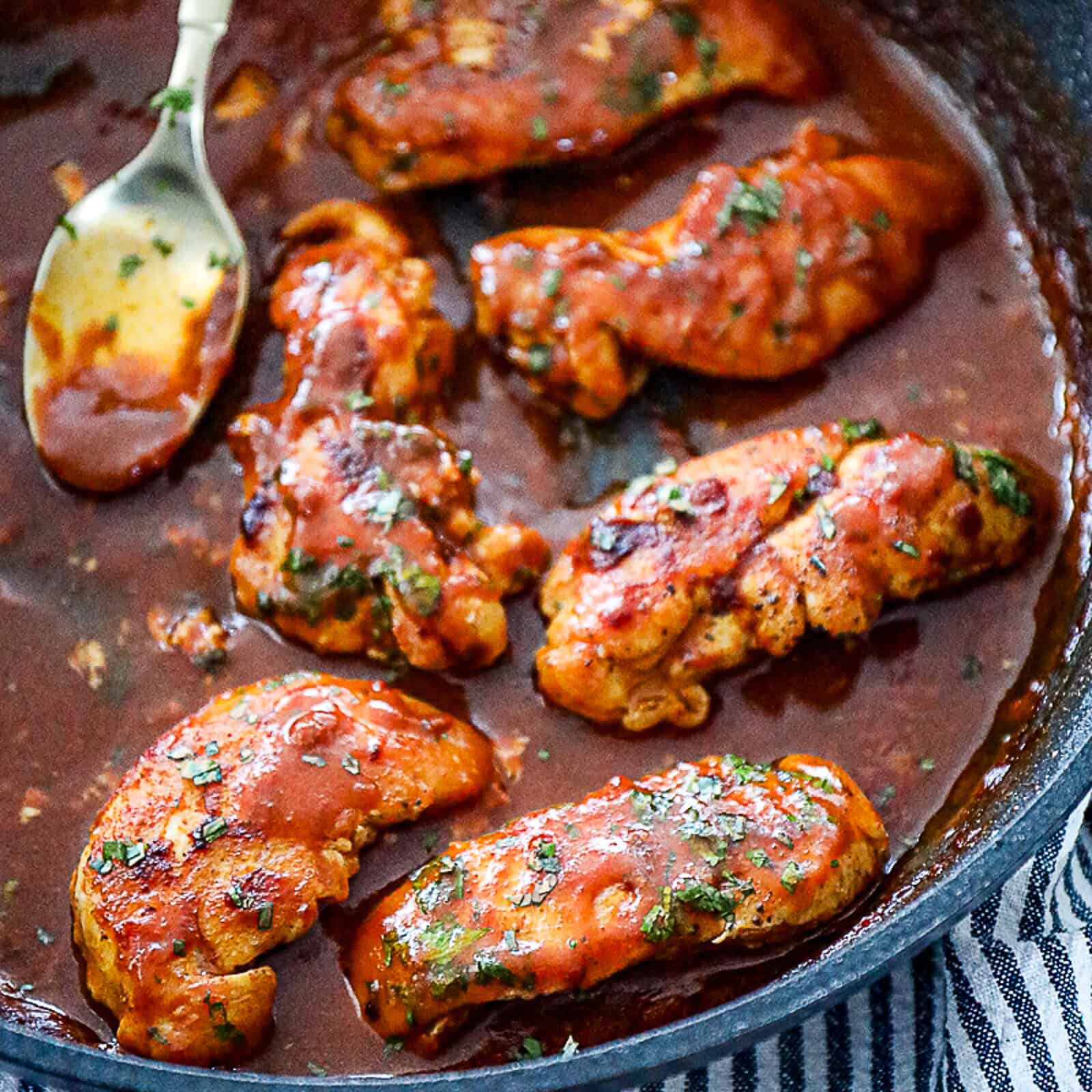 Cooked chicken tenderloins simmering in enchilada sauce in a skillet