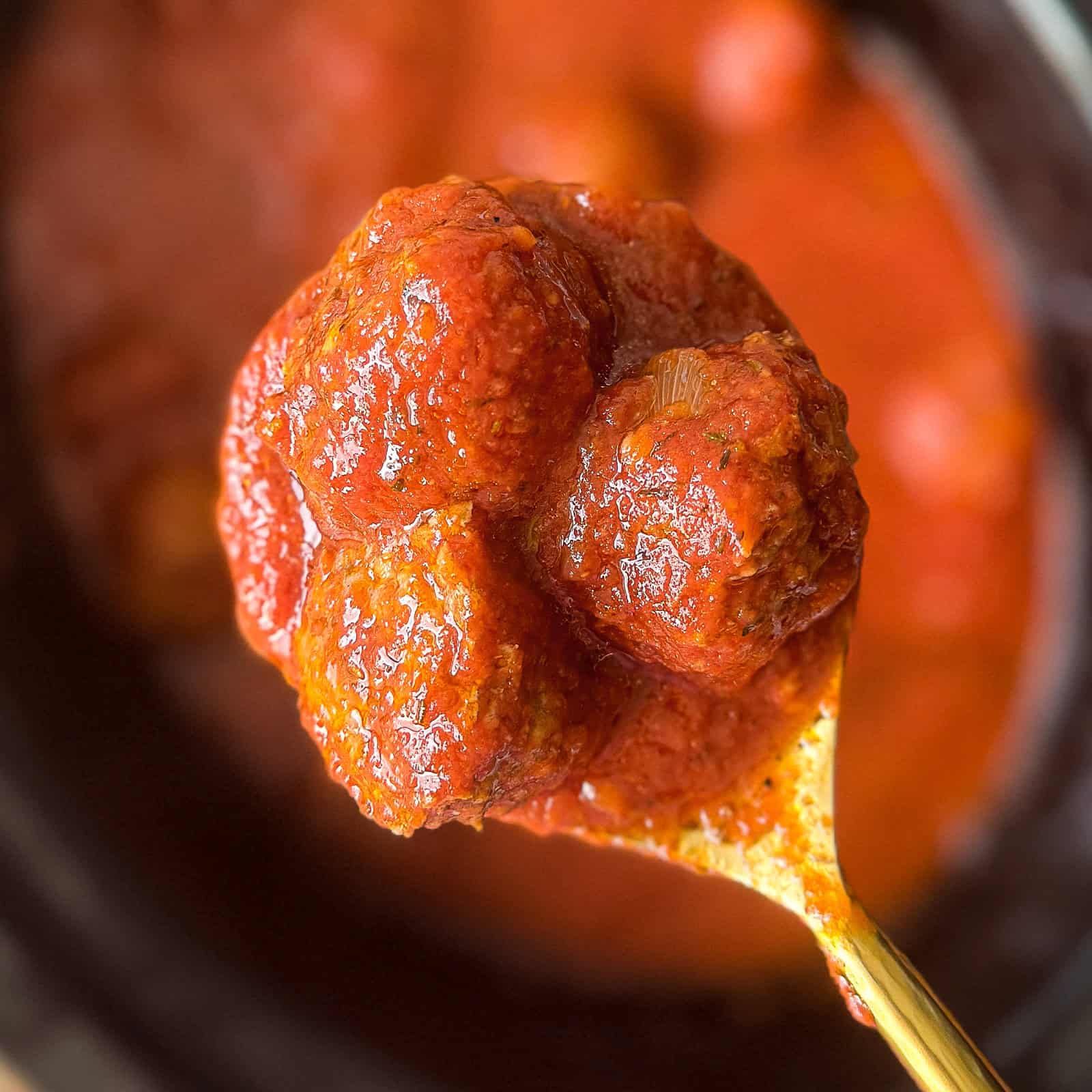 Spoon holding meatballs in tomato sauce above a crock pot