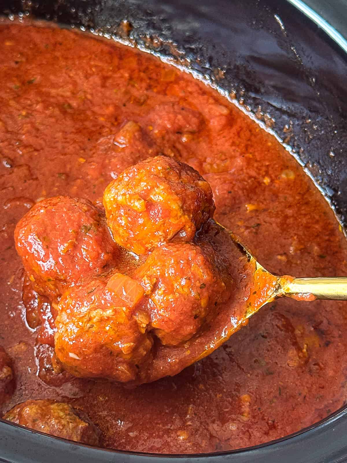 Spoon lifting slow cooked meatballs coated in rich tomato sauce