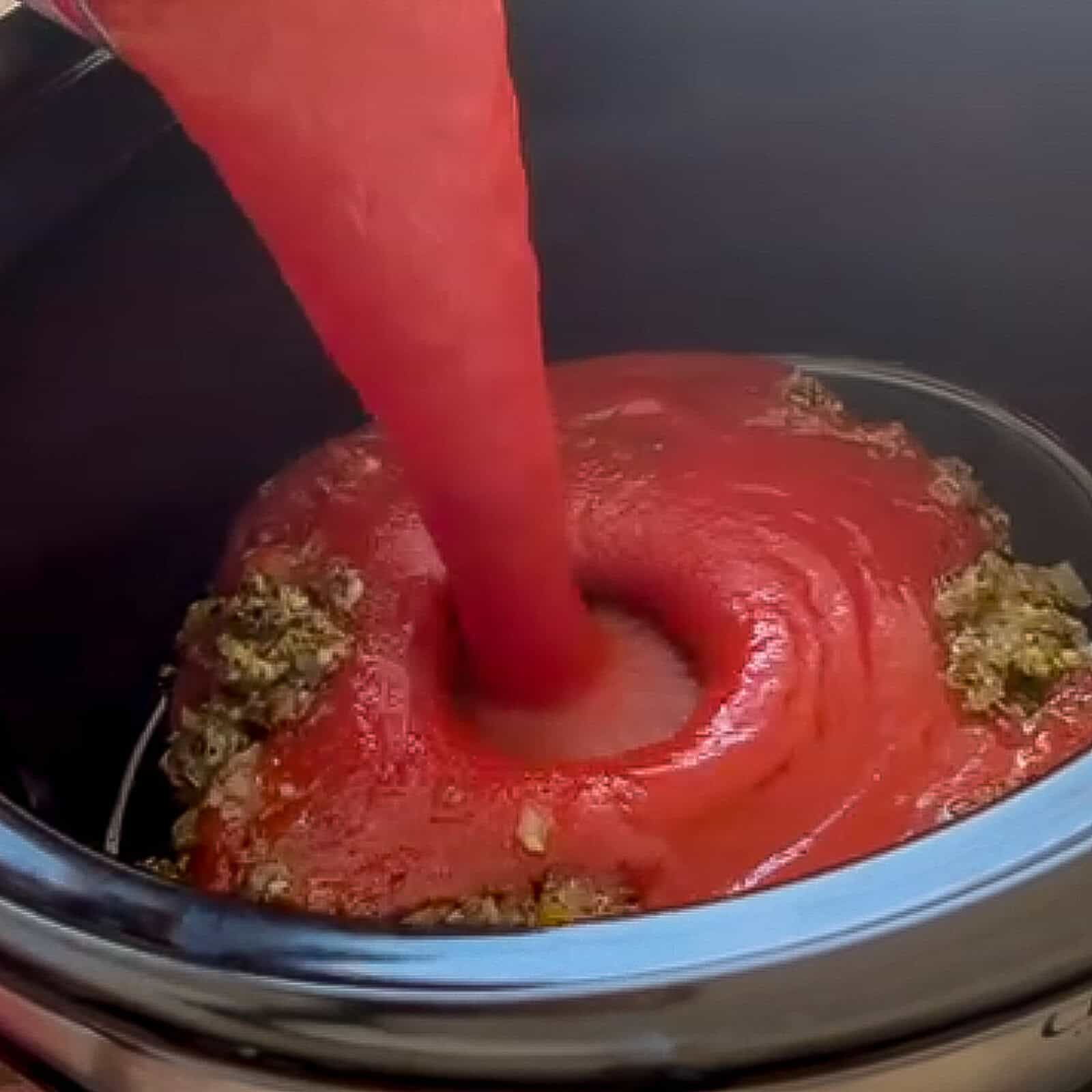 Pouring tomato sauce over sautéed onion and garlic mixture in a slow cooker