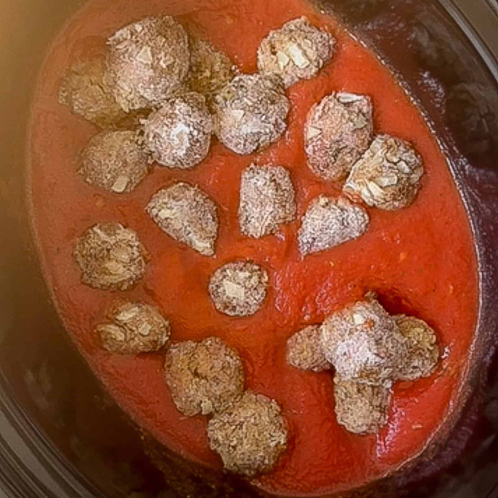 Baked meatballs covered in tomato sauce inside a slow cooker