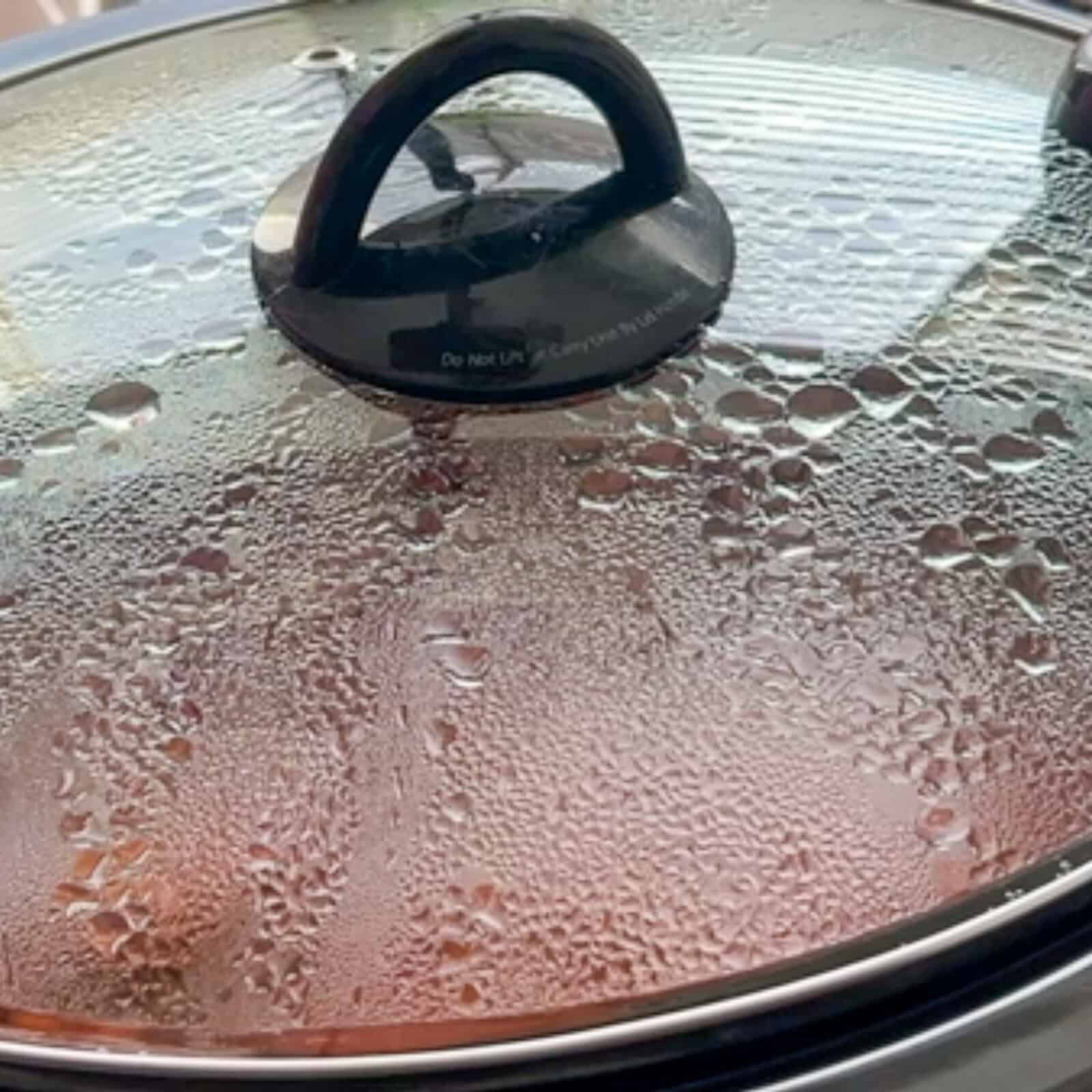 Lid on slow cooker showing meatballs simmering in tomato sauce