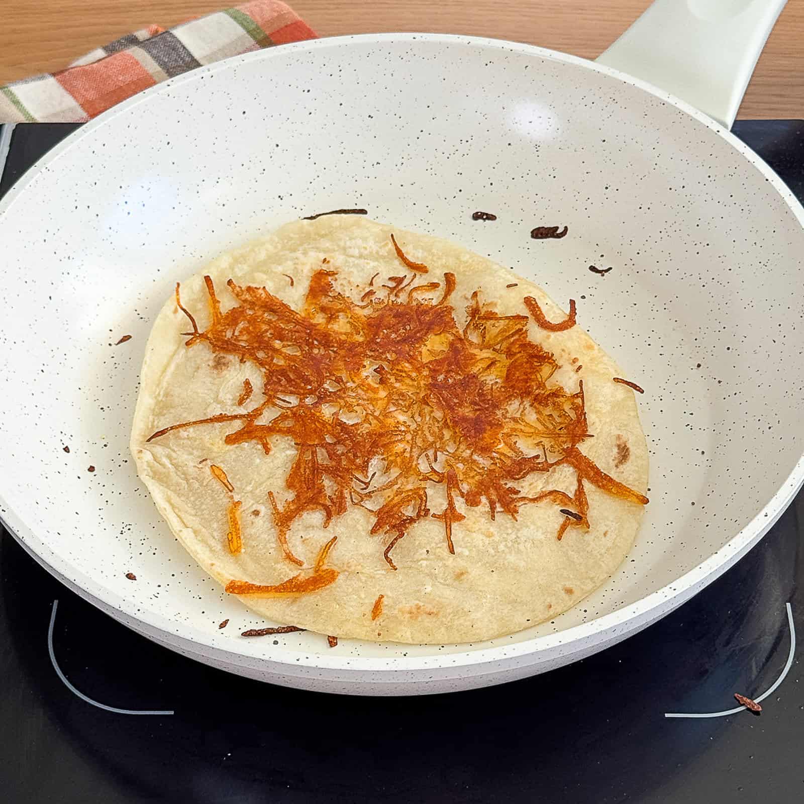 Cheesy tortilla cooking in a pan until bubbly and golden