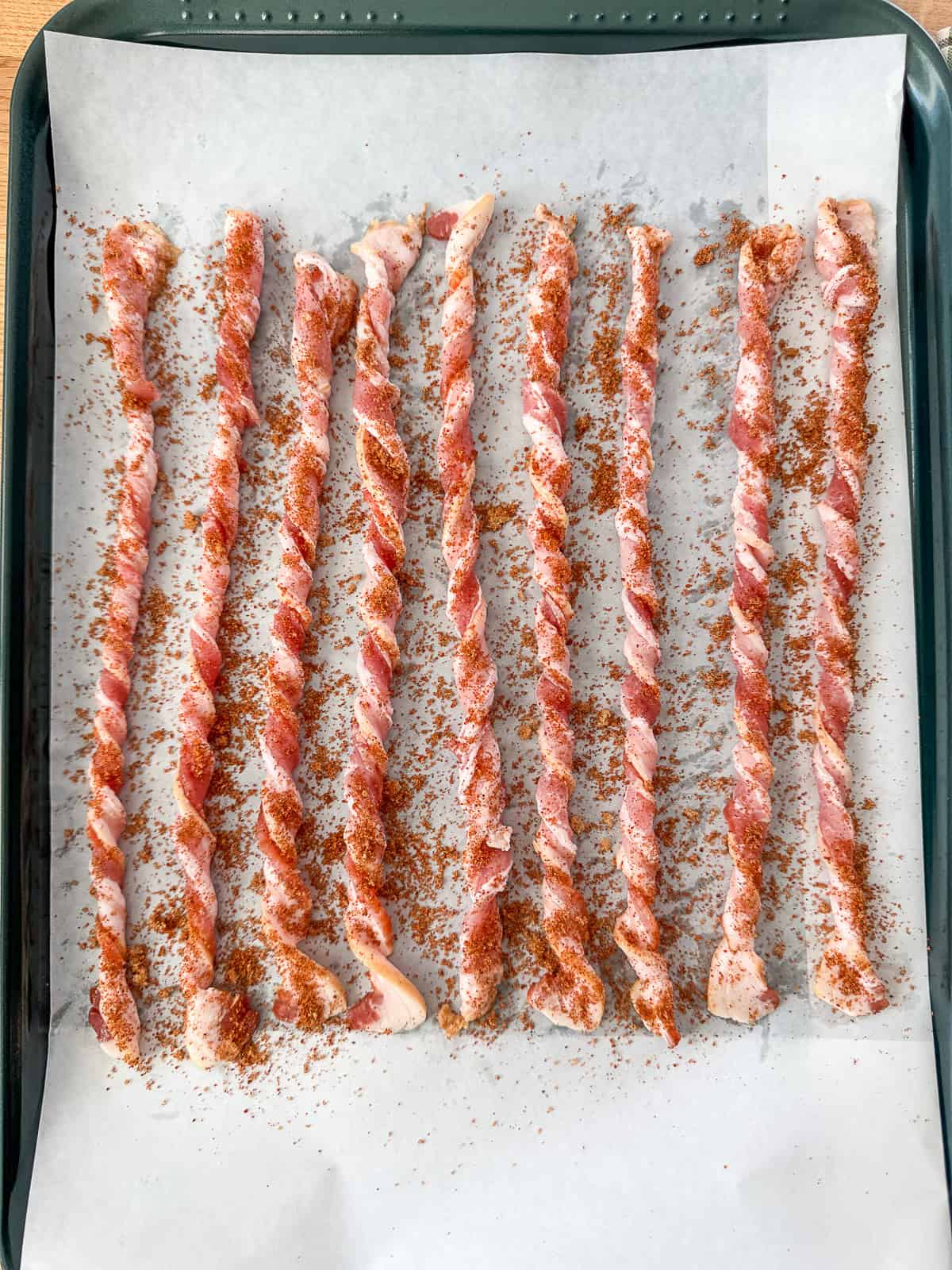 Prepped BBQ Twisted Bacon neatly arranged on a parchment-lined baking sheet ready for the oven