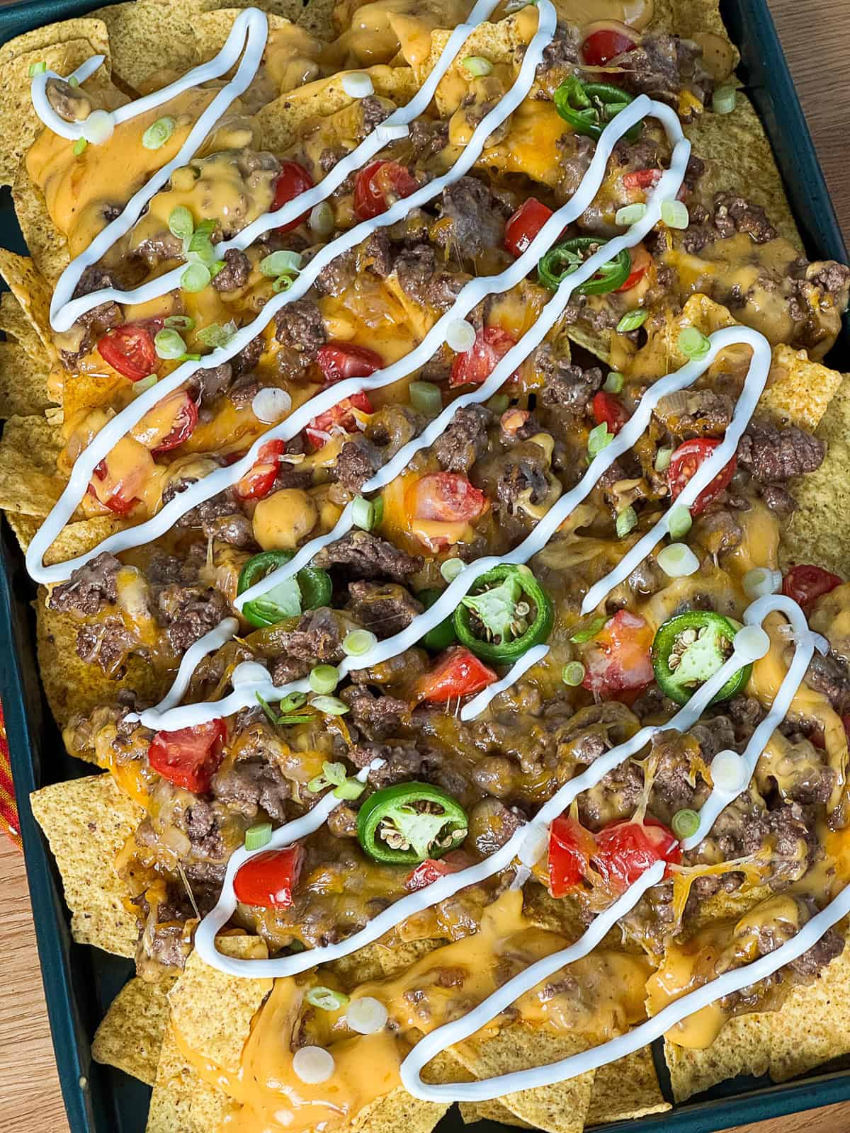 Sour cream–topped viral sheet pan nachos with sliding cheese, tomatoes, jalapeños, and ground beef